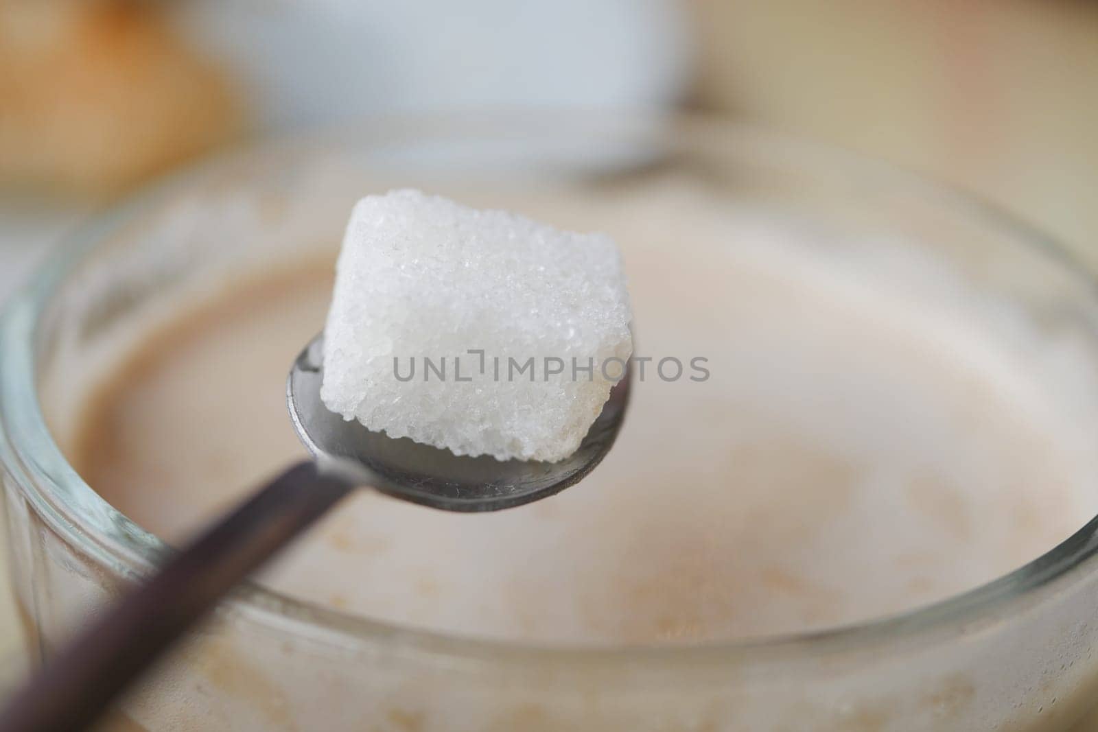 A hand delicately holding a sugar cube high above a steaming cup of rich coffee