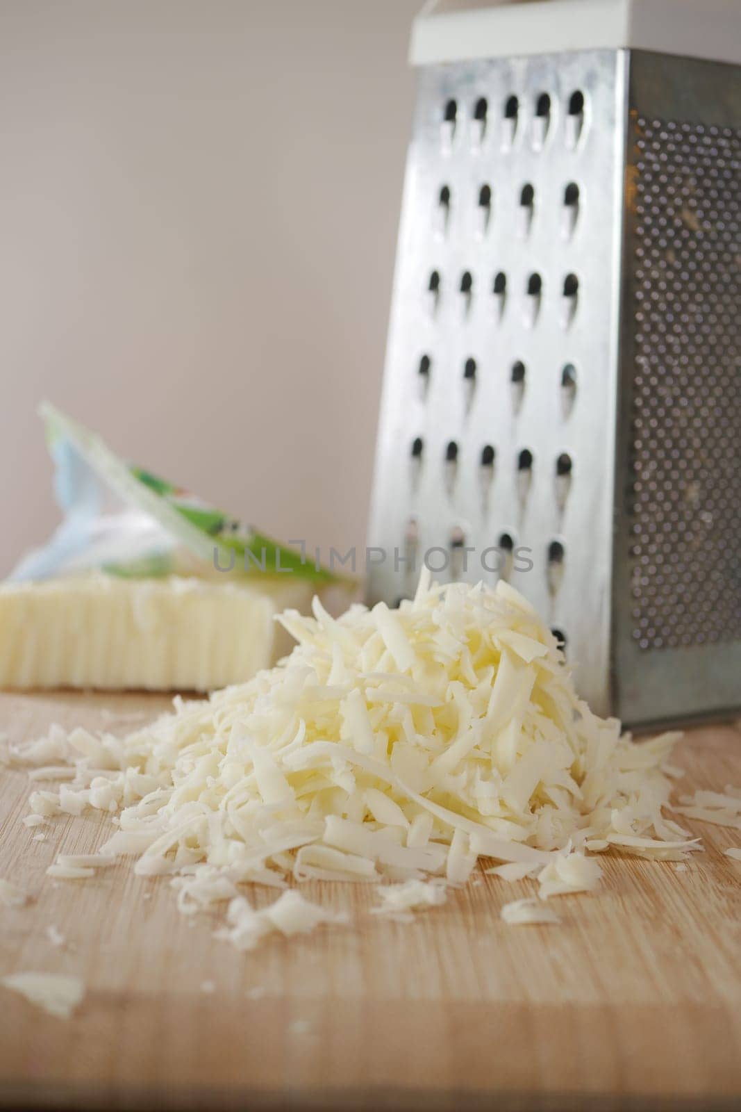 Freshly grated cheese beautifully piled next to a metal grater resting on a wooden surface