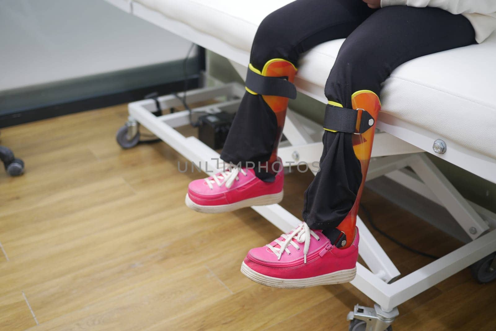 Child's Legs With Orthopedic Braces and Bright Pink Shoes on Clinic Bed.