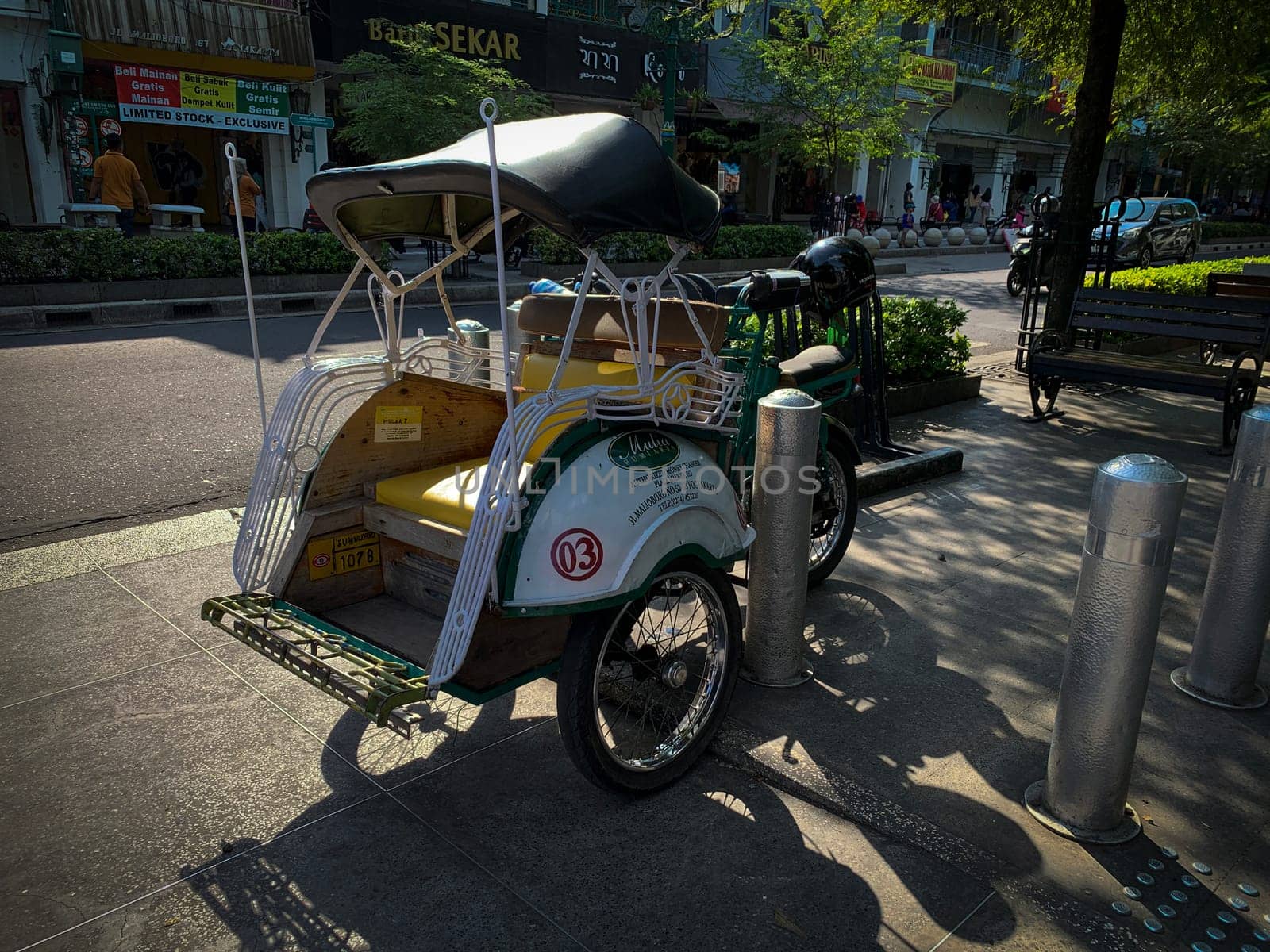 pedicab or rickshaw or locals calls it becak with a canopy is parked on a sunny street, reflecting a vibrant urban scene. The vehicle features a padded seat and unique design