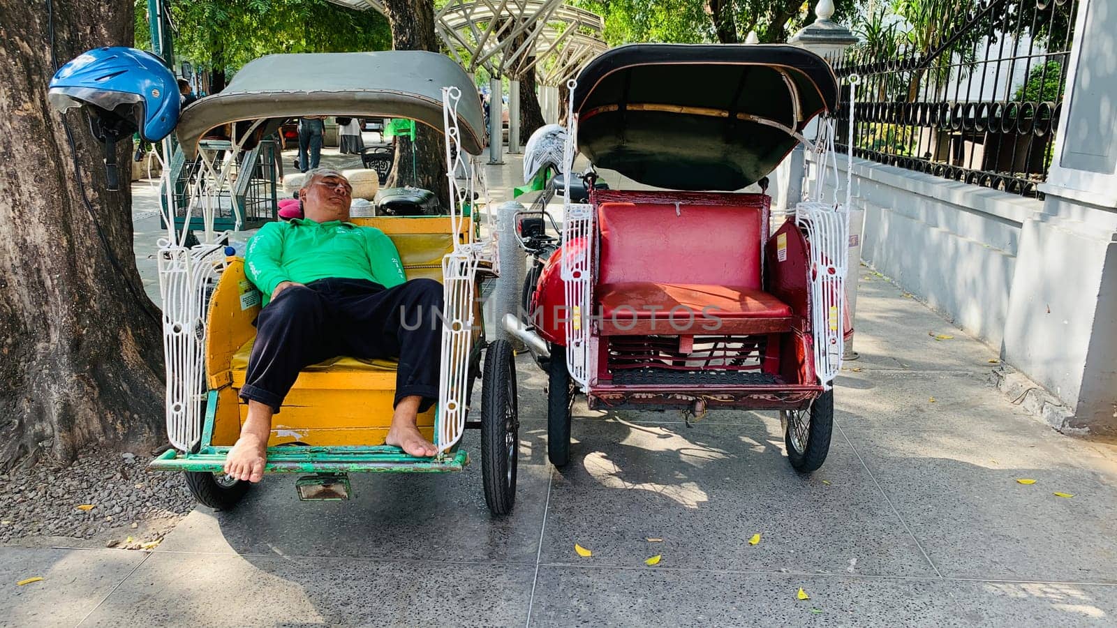 pedicab or rickshaw or locals calls it becak with a canopy is parked on a sunny street, reflecting a vibrant urban scene. The vehicle features a padded seat and unique design