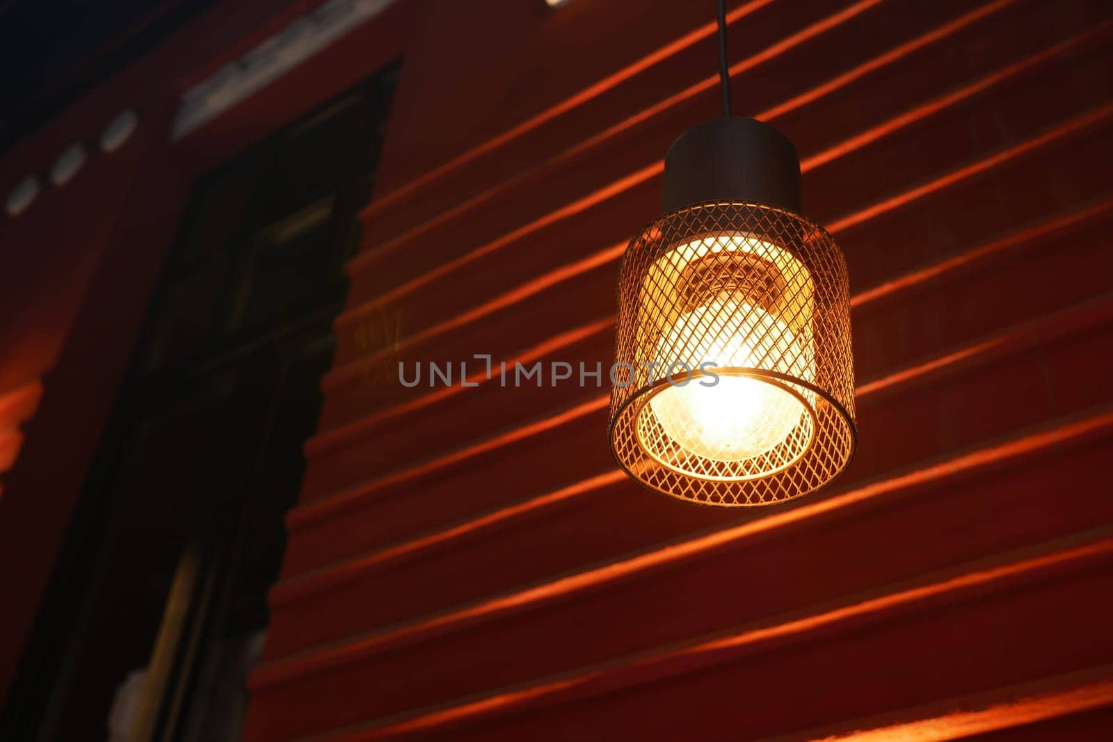 A contemporary hanging light fixture is casting a warm and inviting glow against a vibrant red wall