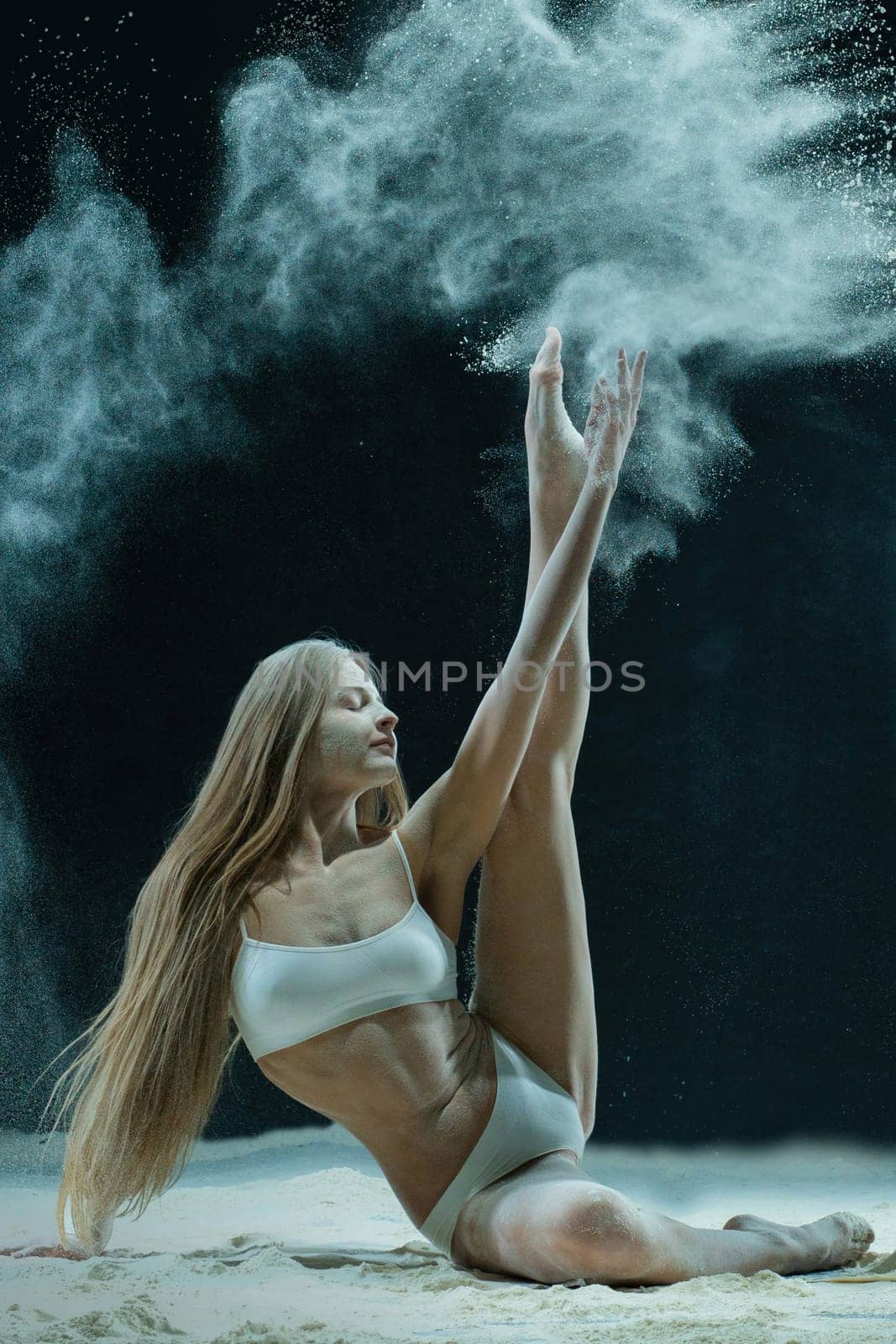 Young blonde sitting in white dust cloud shot in the dark room