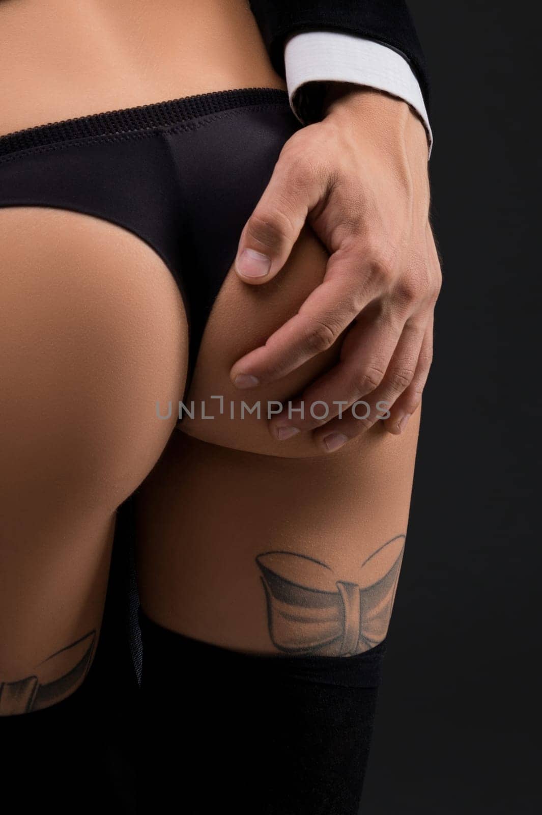 Back view of sexy woman in panties hugging handsome man in black suit and whispering in ear