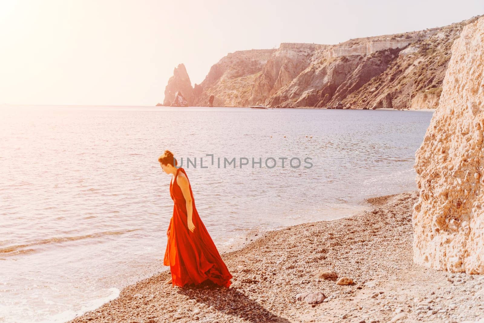 Woman red dress sea. Female dancer in a long red dress posing on a beach with rocks on sunny day. Girl on the nature on blue sky background