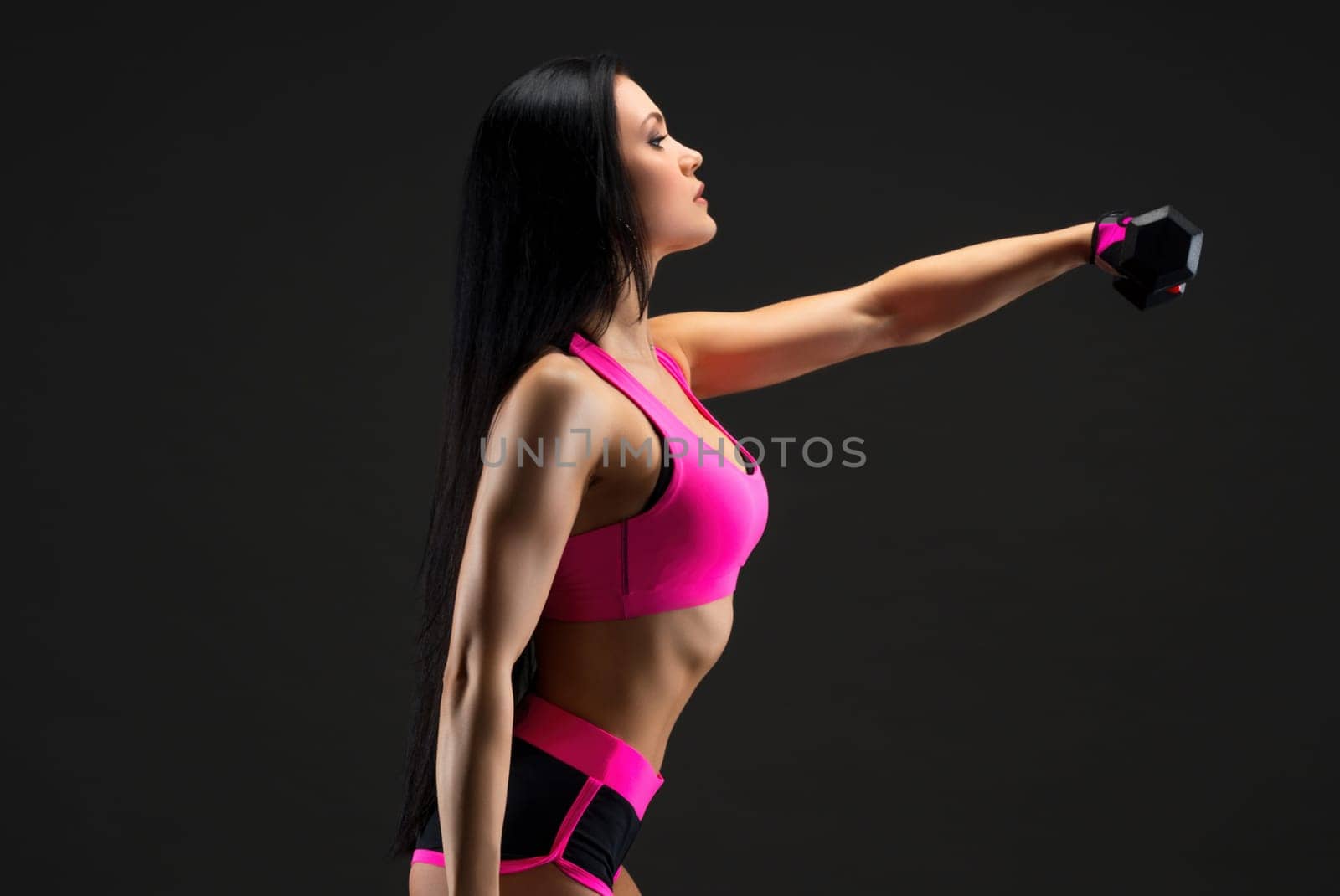 Slim brunette wearing pink top and shorts doing fitness with dumbells profile full-length view