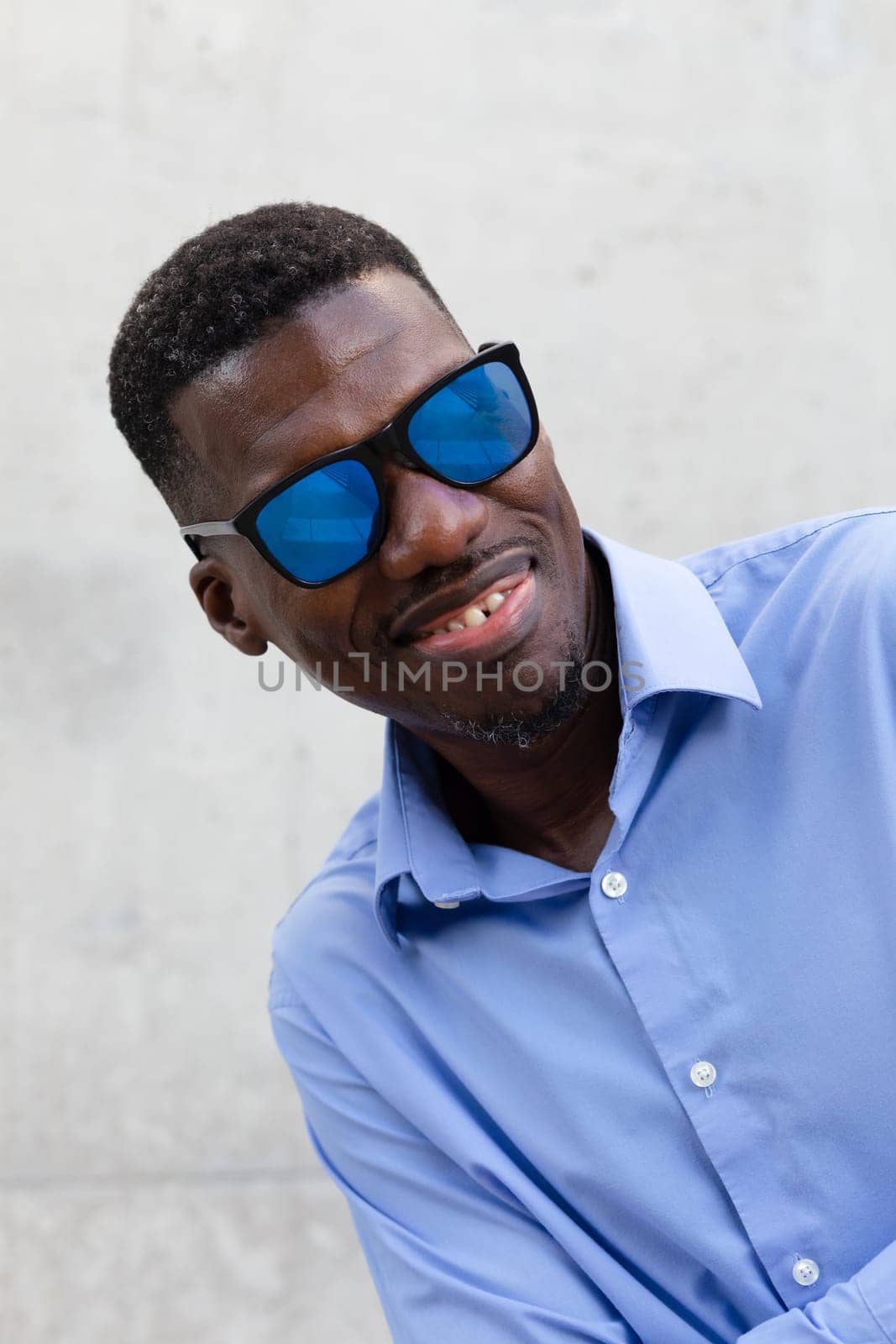 Smiling African American Man In His 40s With Blue Sunglasses And Shirt. Portrait Of Happy Stylish Middle Age Male, Gray Concrete On Background. Accessories. Vertical Plane. High quality photo