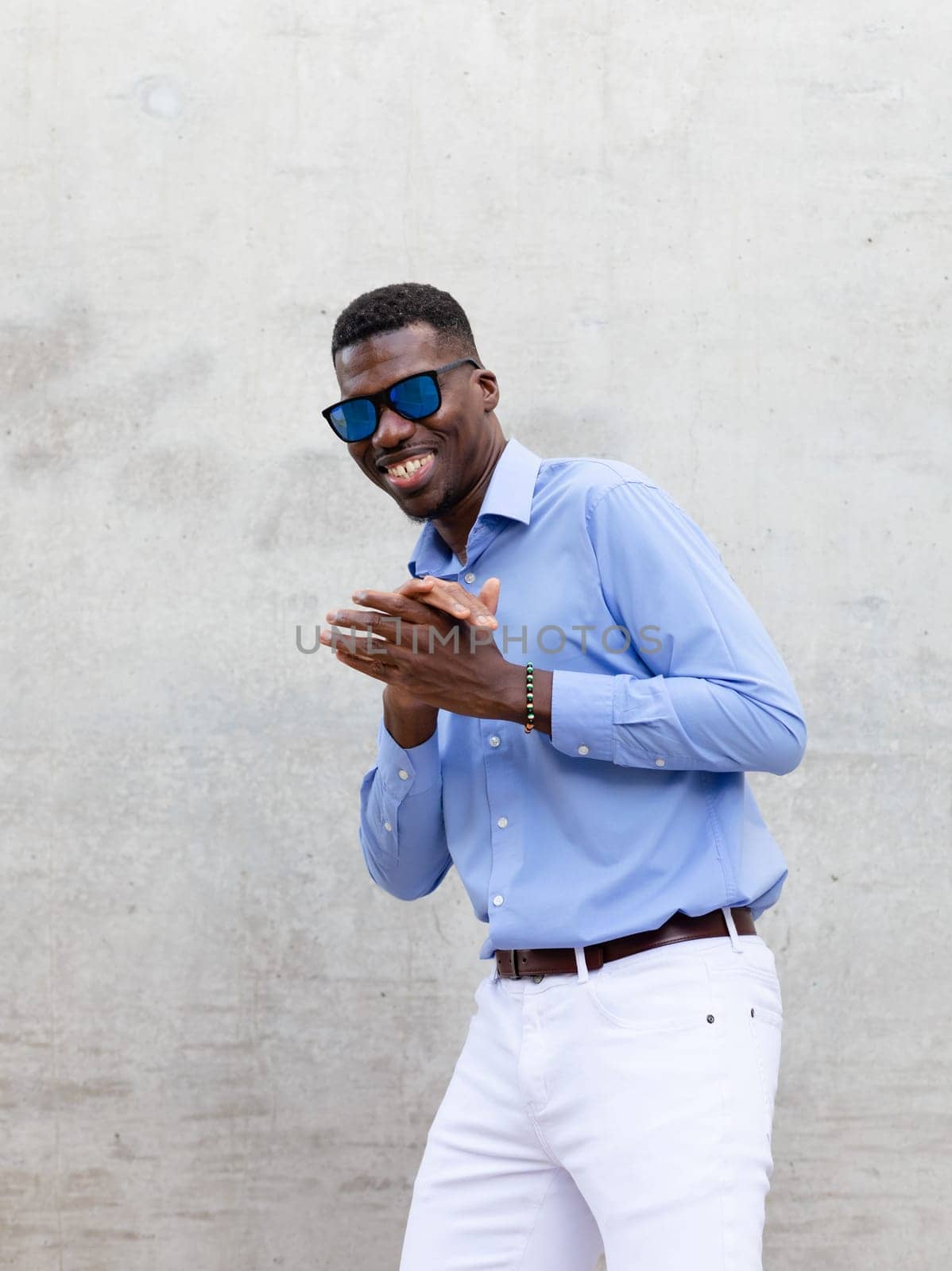 Portrait Cheerful Playful Smiling African American Man In His 40s With Blue Sunglasses And Shirt. Portrait Of Happy Stylish Middle Age Male, Gray Concrete On Background. Accessories. Vertical Plane.