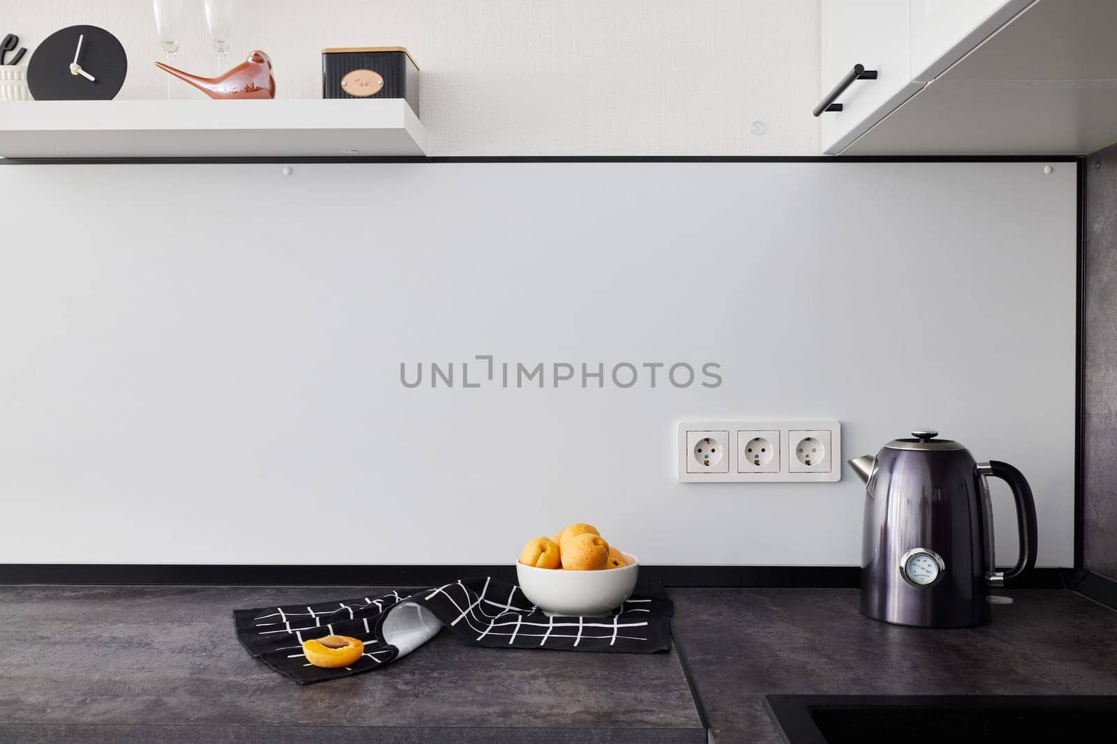 This stylish kitchen features vibrant citrus fruits, an electric kettle, and a sleek, contemporary design