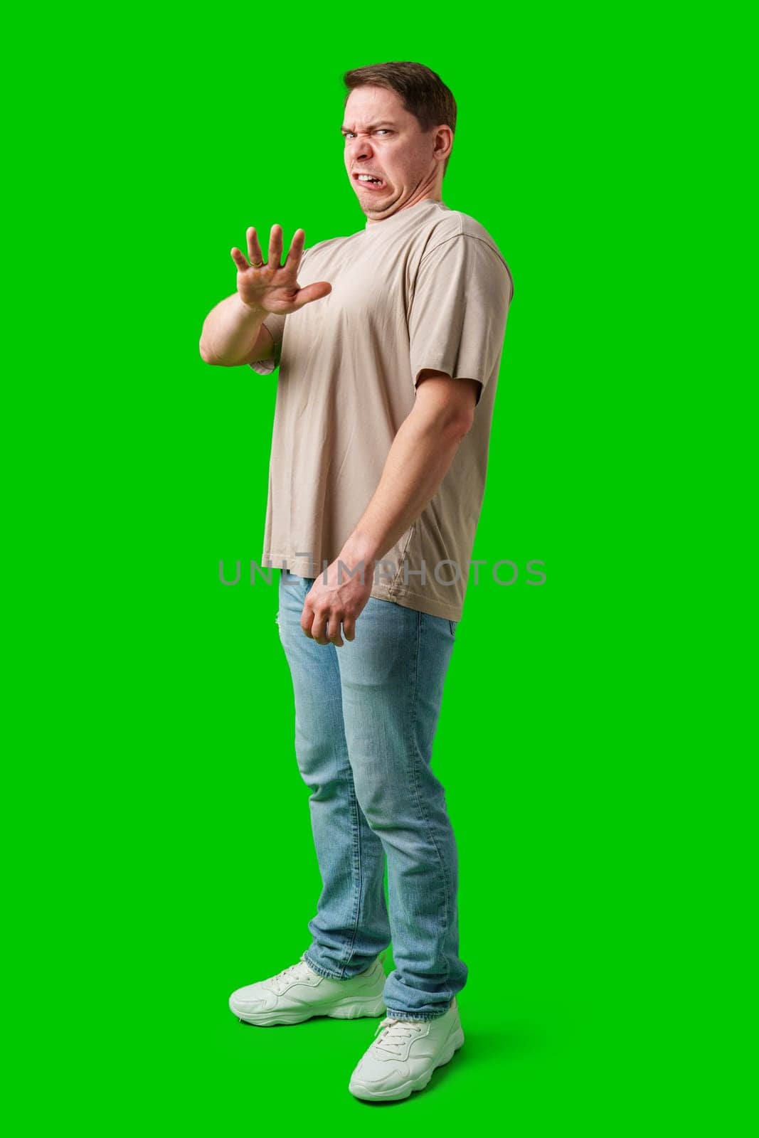 Young man making a disgusted expression while standing against a bright green background in studio