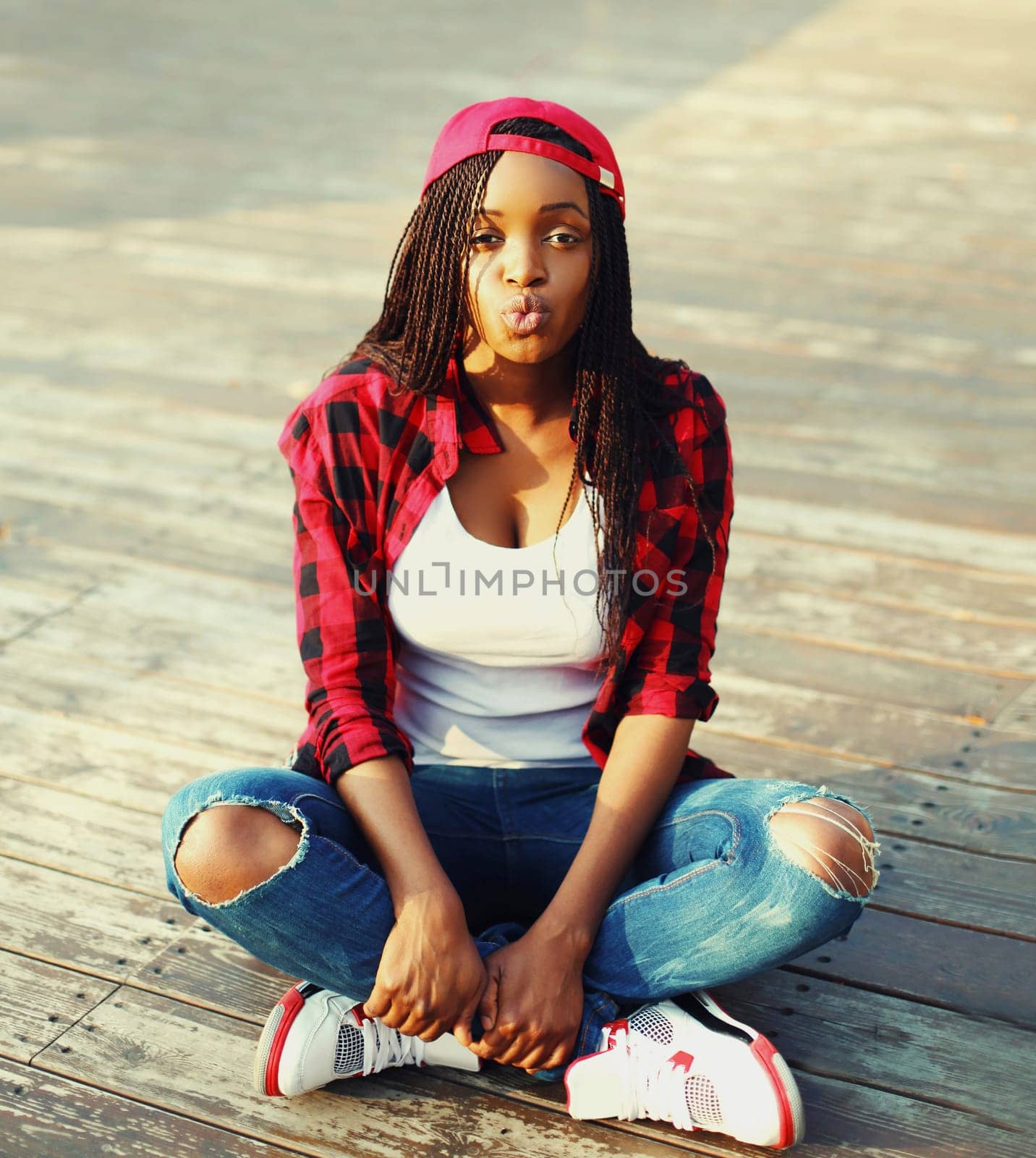 Fashion young african woman is having fun in the city, wearing red checkered shirt and baseball cap