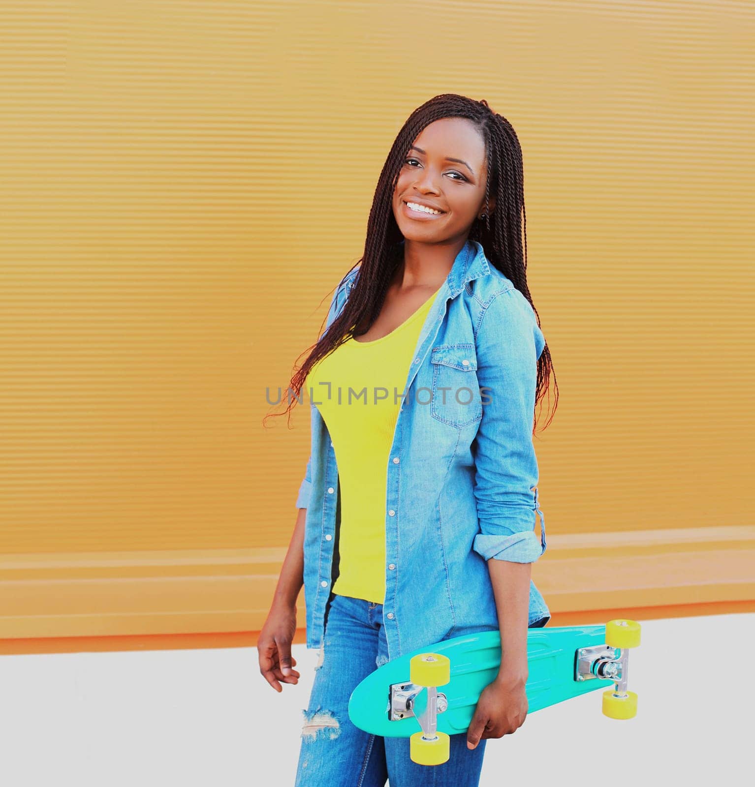 Portrait of happy smiling young african woman model posing with skateboard in the city