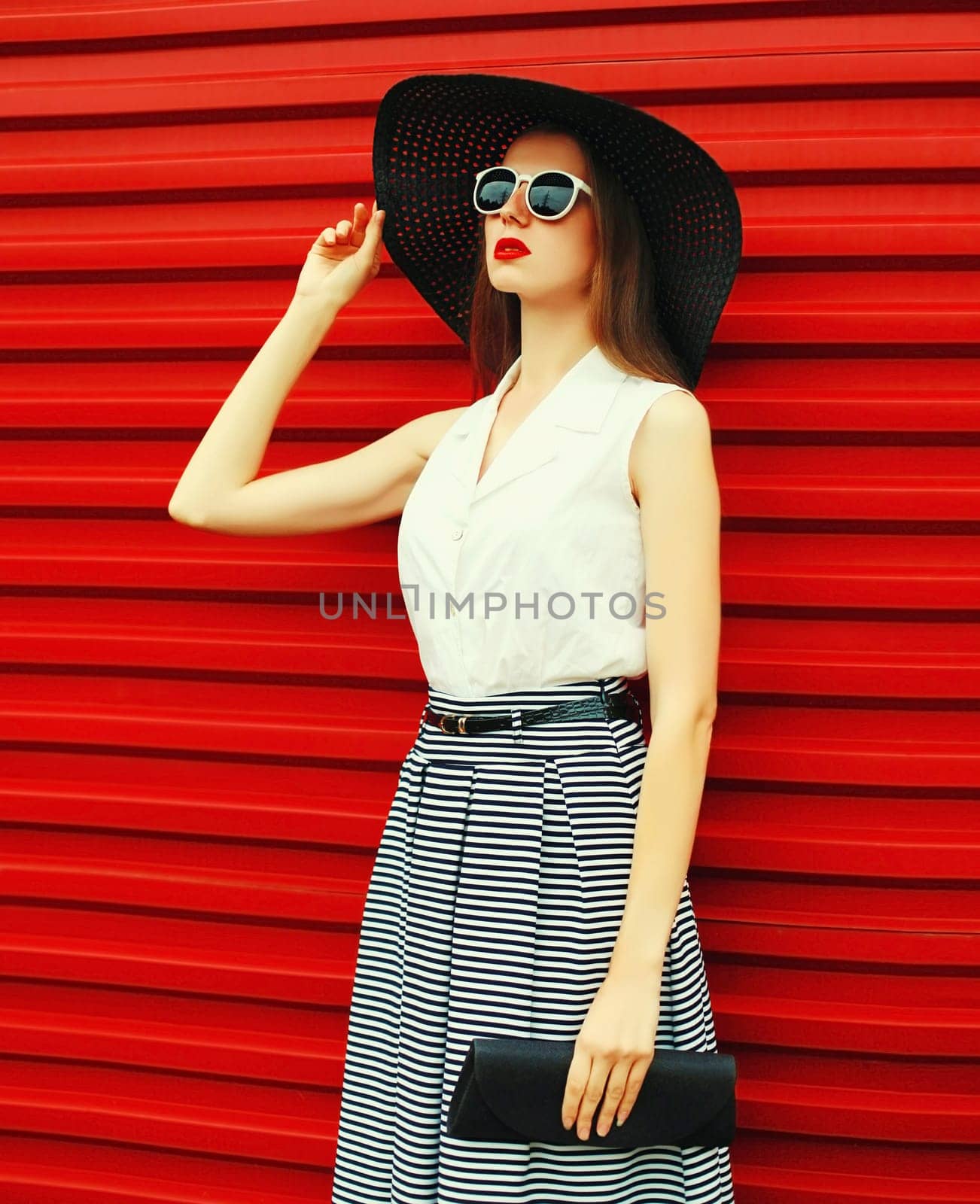 Portrait of stylish young woman model posing wearing summer round hat, handbag on red background