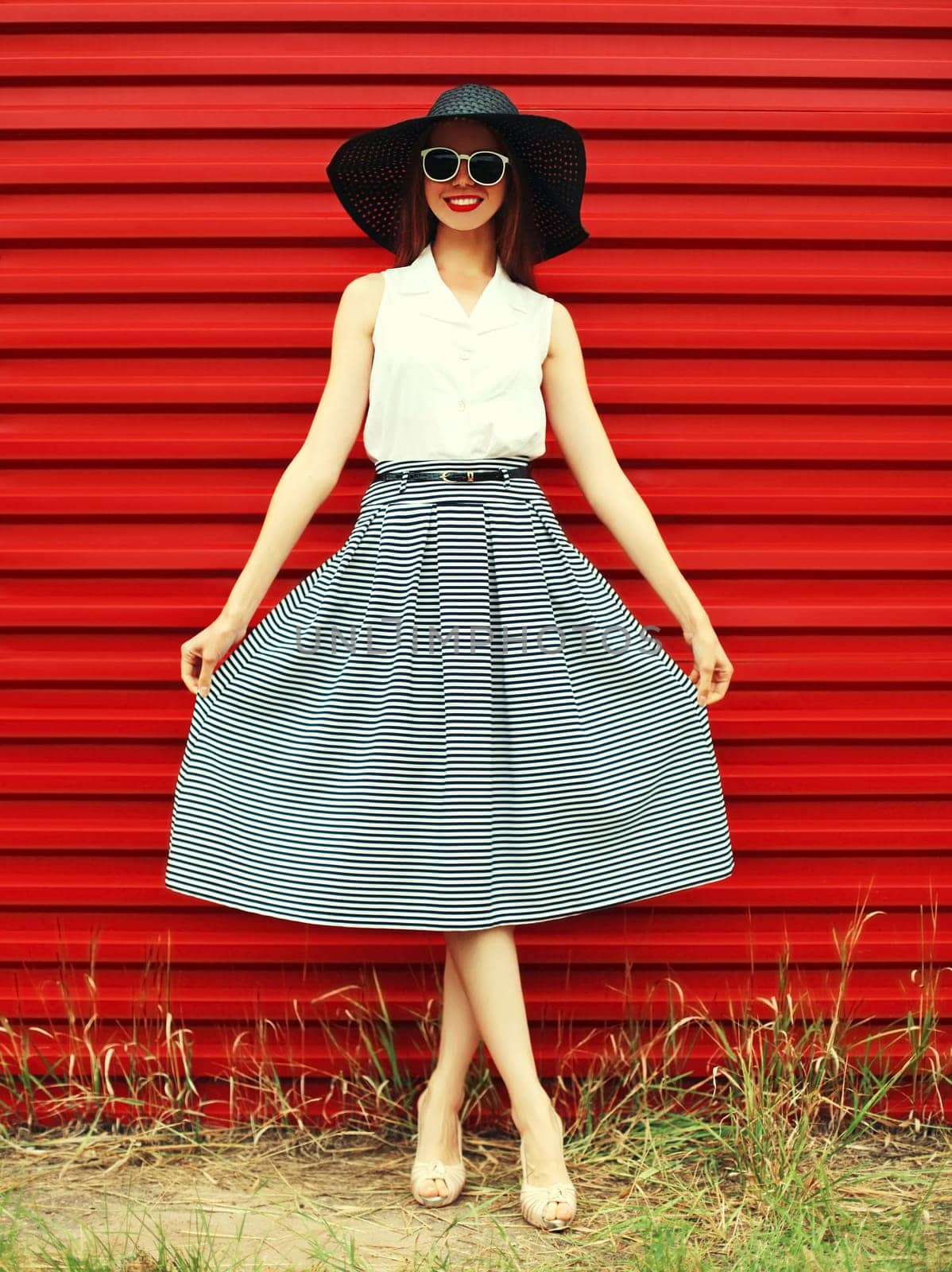 Portrait of stylish young woman model posing wearing black summer straw round hat on red background