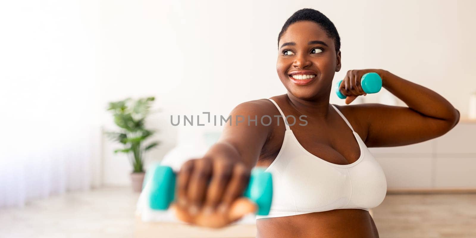 Home sports for weight loss. Happy plus size black woman doing fitness exercises with dumbbells indoors. Millennial overweight lady strengthening her biceps, leading active lifestyle