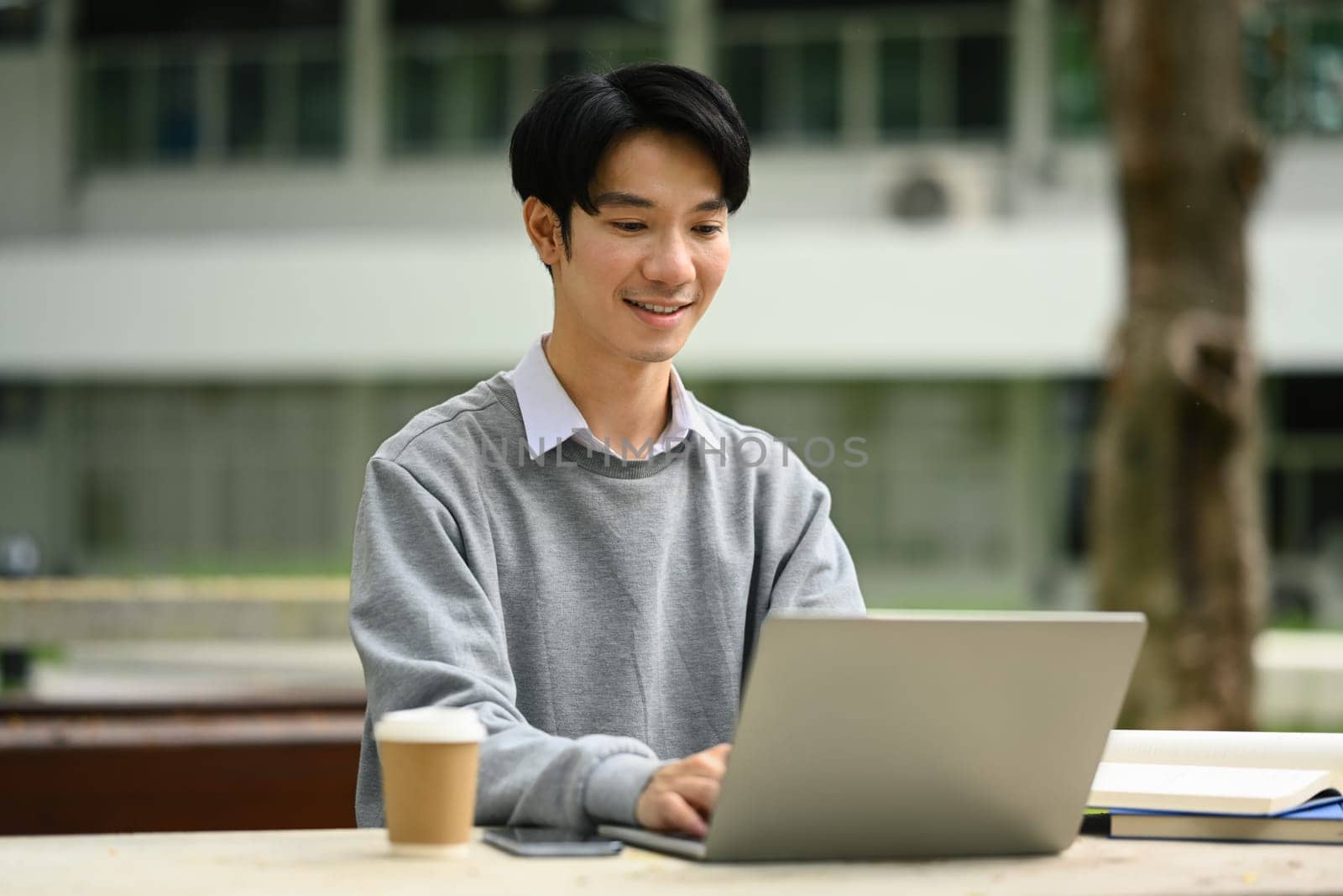 Handsome man using laptop, preparing for exam on table at campus. Youth lifestyle and education concept.