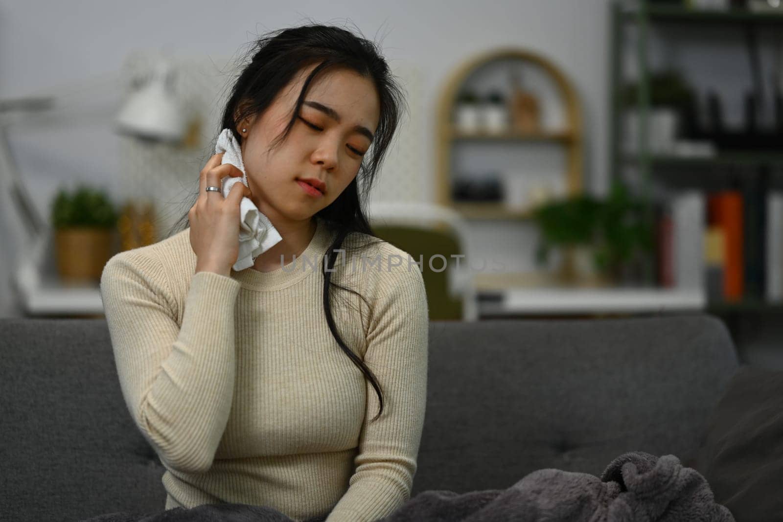 Sick young woman wiping her face with wet towel for reduce high fever. Illness and health care concept.