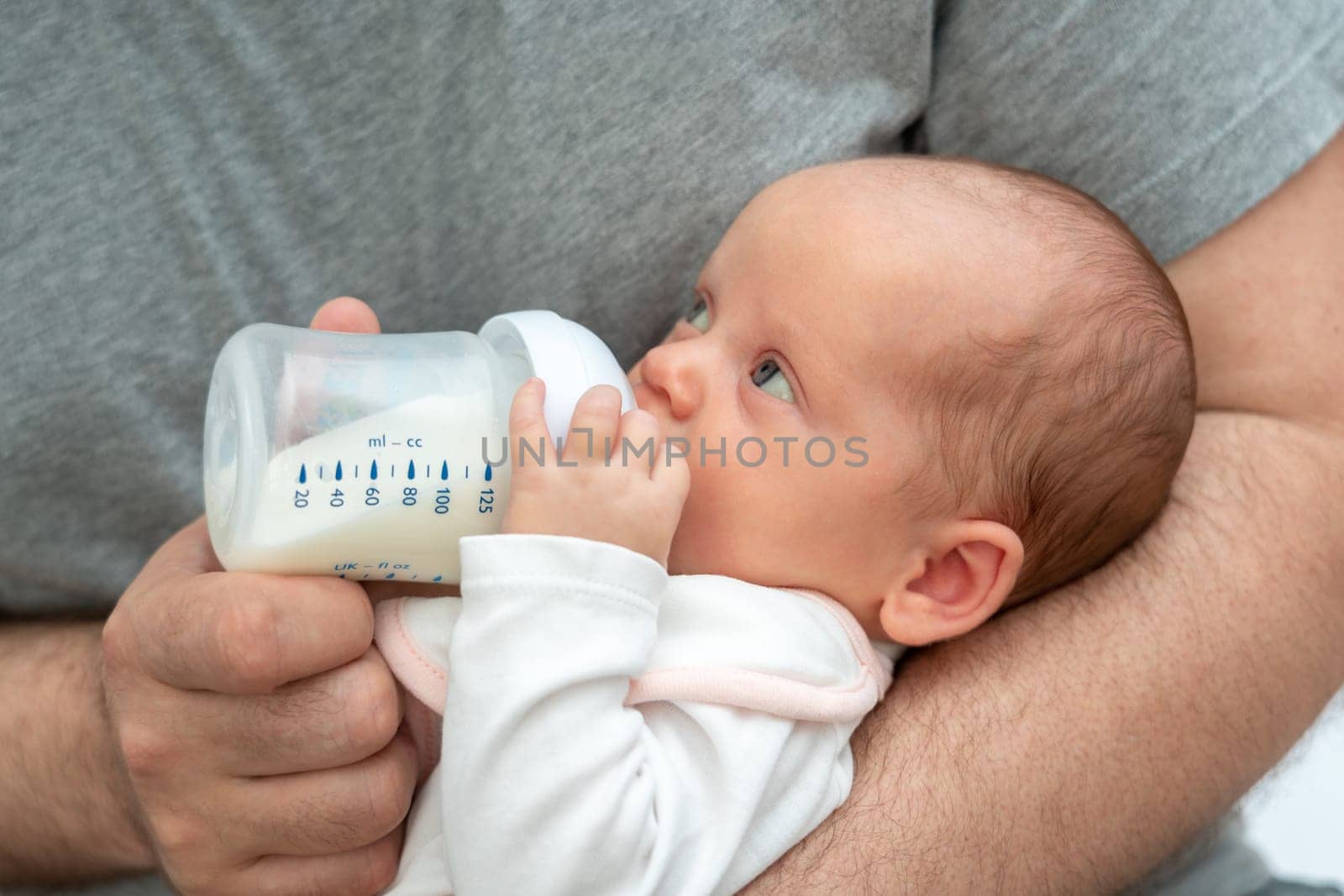 A man embarks on the rewarding journey of fatherhood, tenderly feeding his baby formula from a