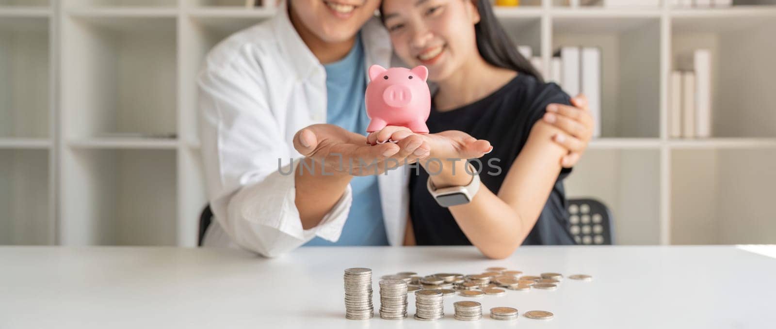 Happy couple asian saving while sitting together on desk at home, loving spouse plan budget and saving money for future.