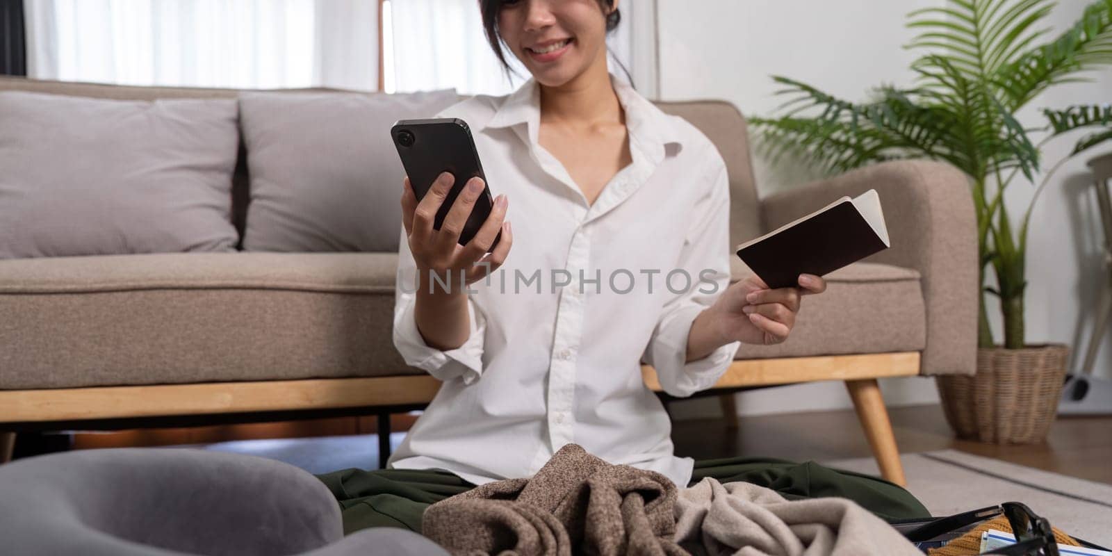 Young traveler woman using smartphone to book a hotel and search for tourist attraction information while prepare travel suitcase before going on summer vacation. Online booking concept.