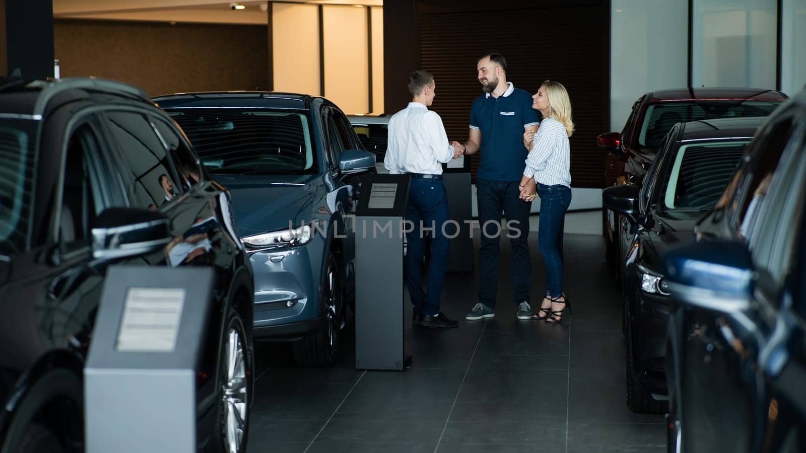 A caucasian couple shakes hands with a salesperson while buying a car