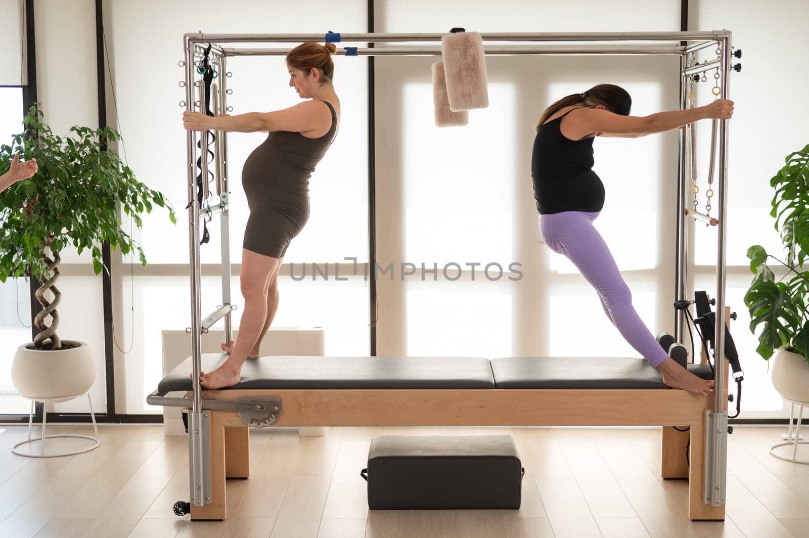 Two pregnant women are doing Pilates on a Cadillac reformer