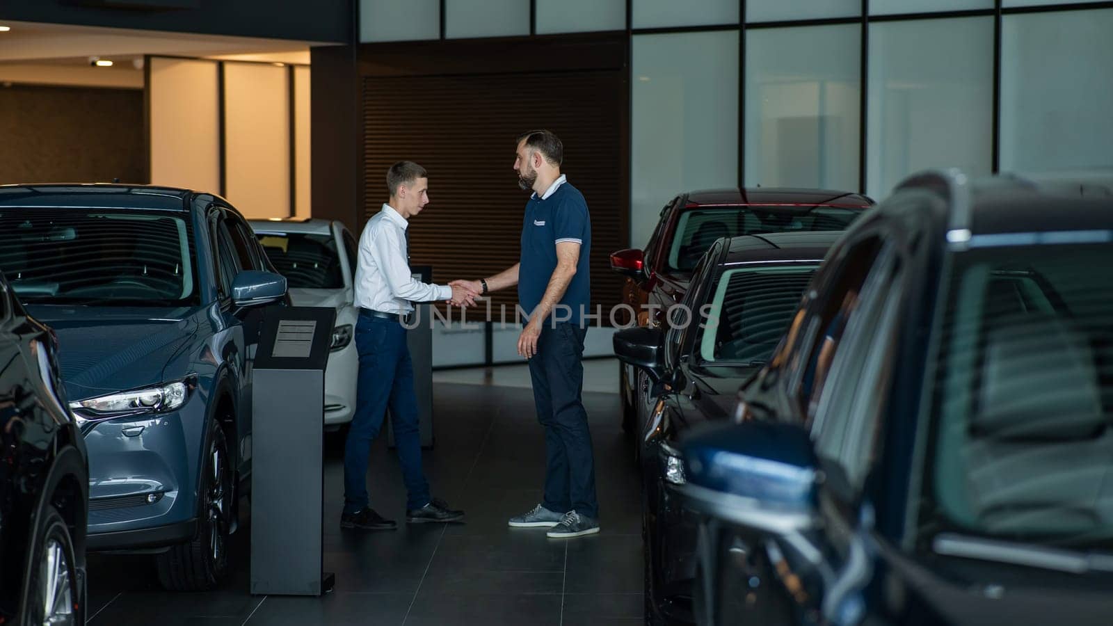 Seller and buyer shake hands in a car dealership. Caucasian man buys a car