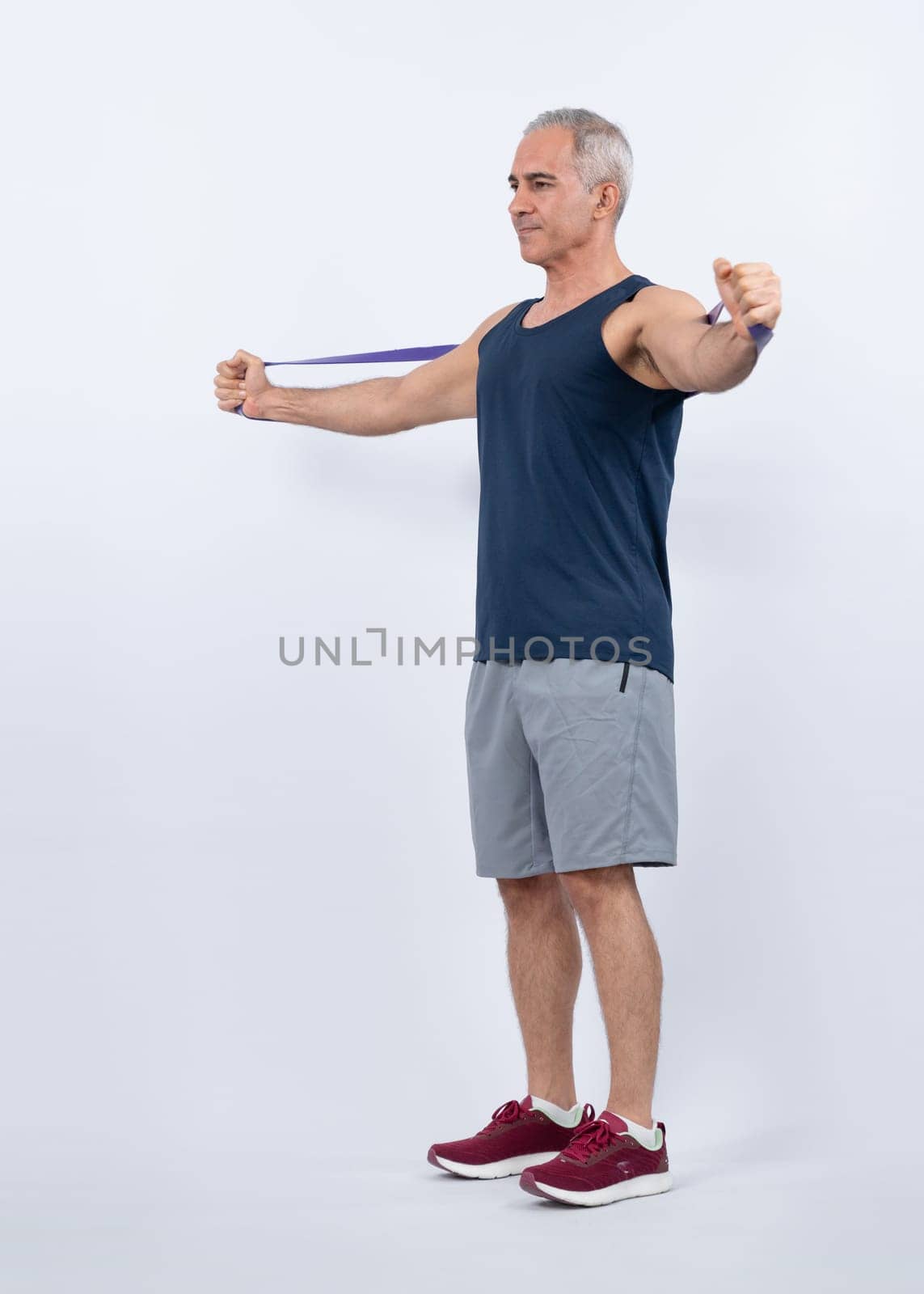 Full body length shot athletic and sporty senior man with fitness resistance band on isolated background. Healthy active physique and body care lifestyle after retirement. Clout