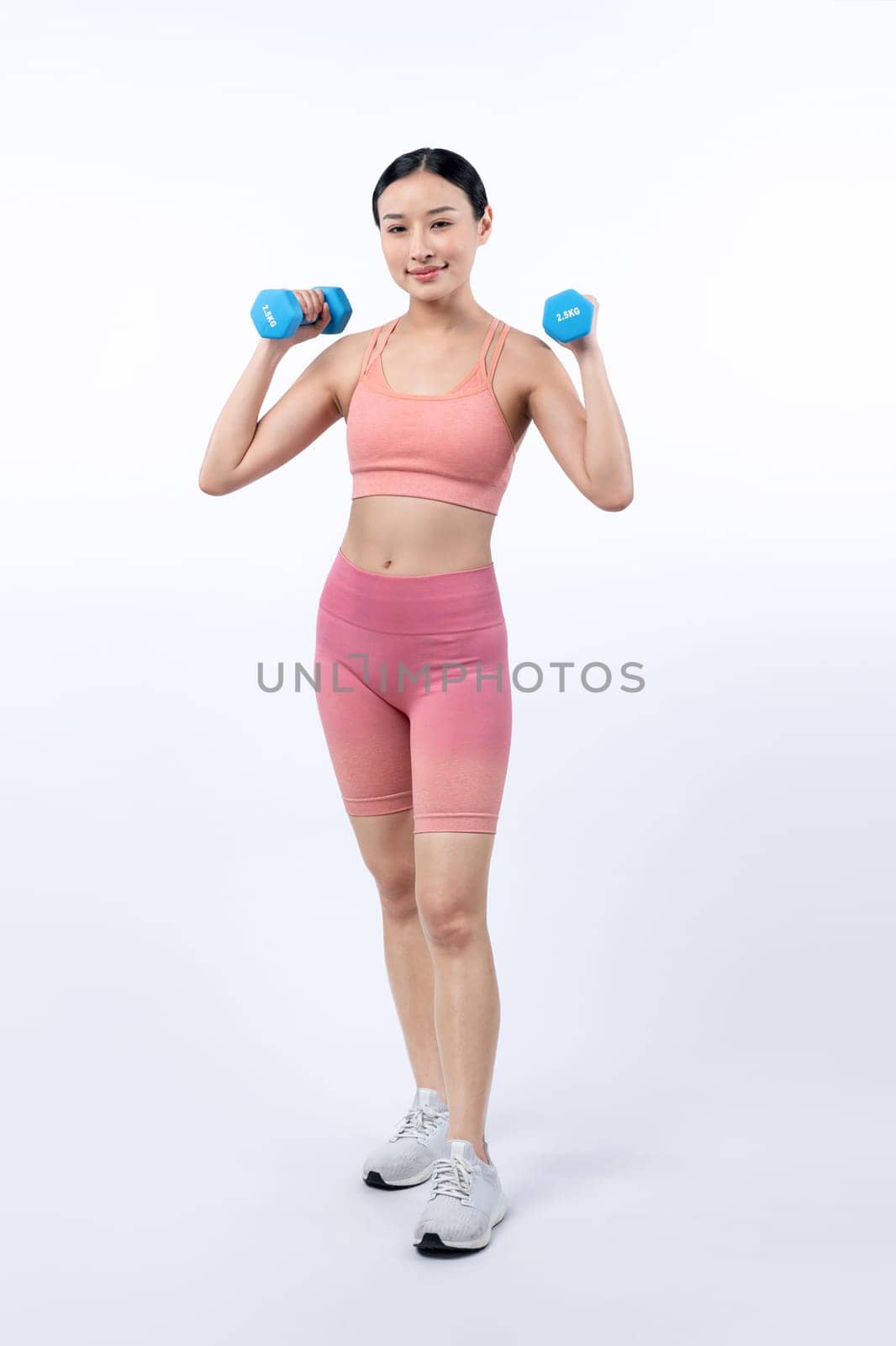 Vigorous energetic woman doing dumbbell weight lifting exercise on isolated background. Young athletic asian woman strength and endurance training session as body workout routine.