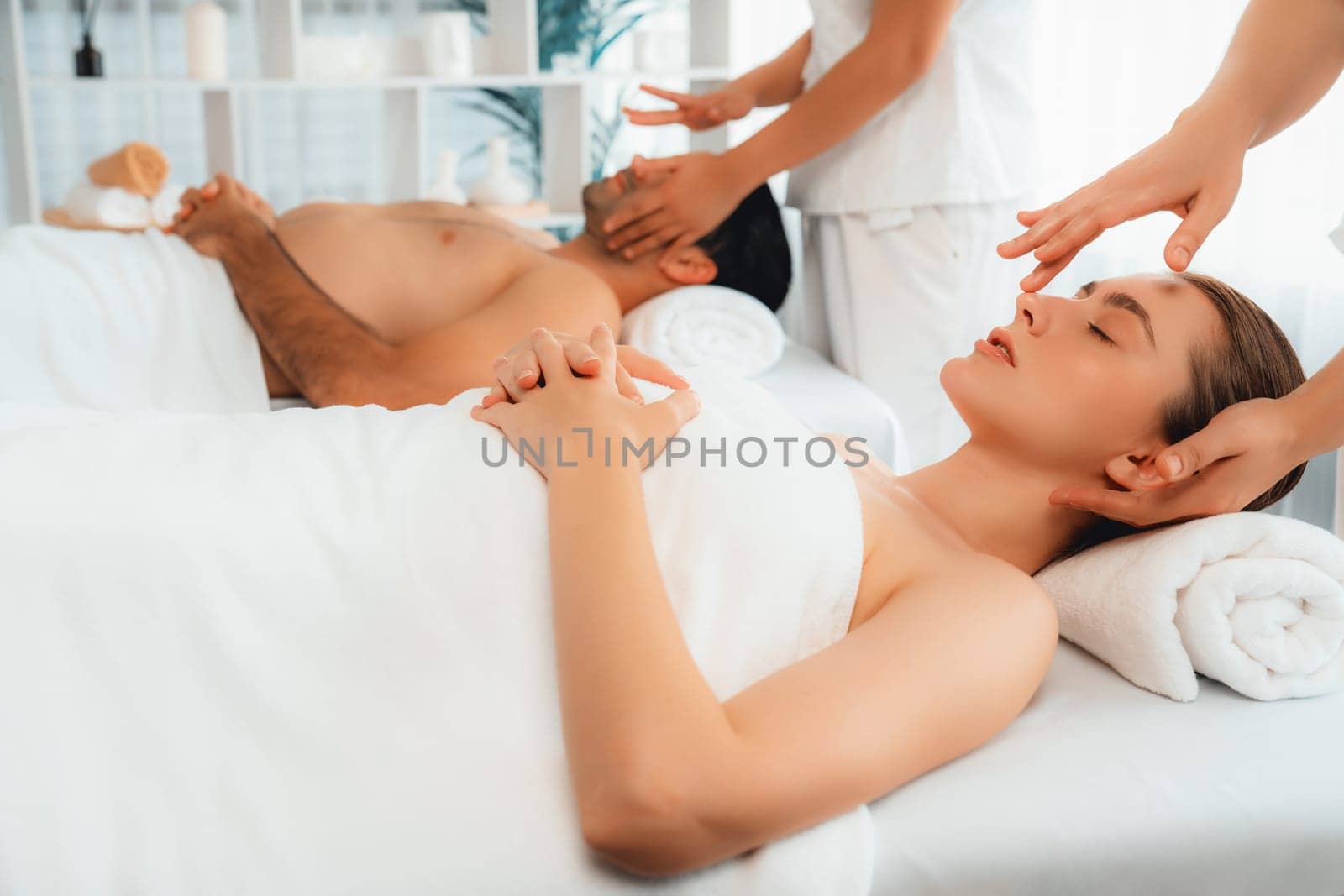 Caucasian couple enjoying relaxing anti-stress head massage and pampering facial beauty skin recreation leisure in dayspa modern light ambient at luxury resort or hotel spa salon. Quiescent