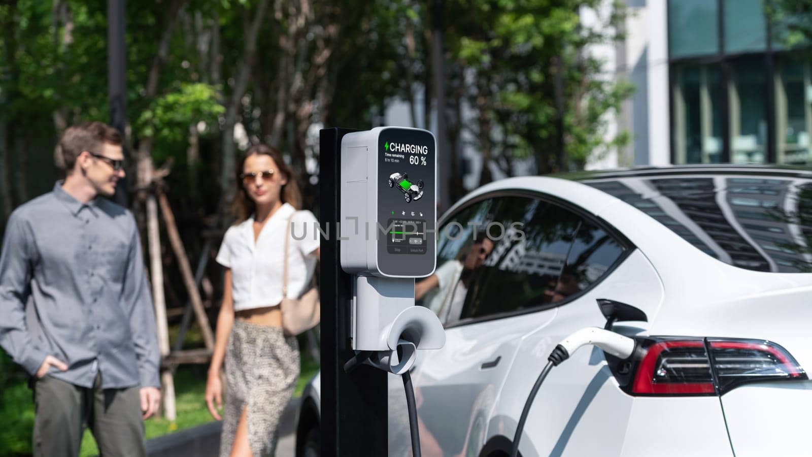 Young couple travel with EV electric car charging in green sustainable city outdoor garden in summer shows urban sustainability lifestyle by green clean rechargeable energy of electric vehicle innards