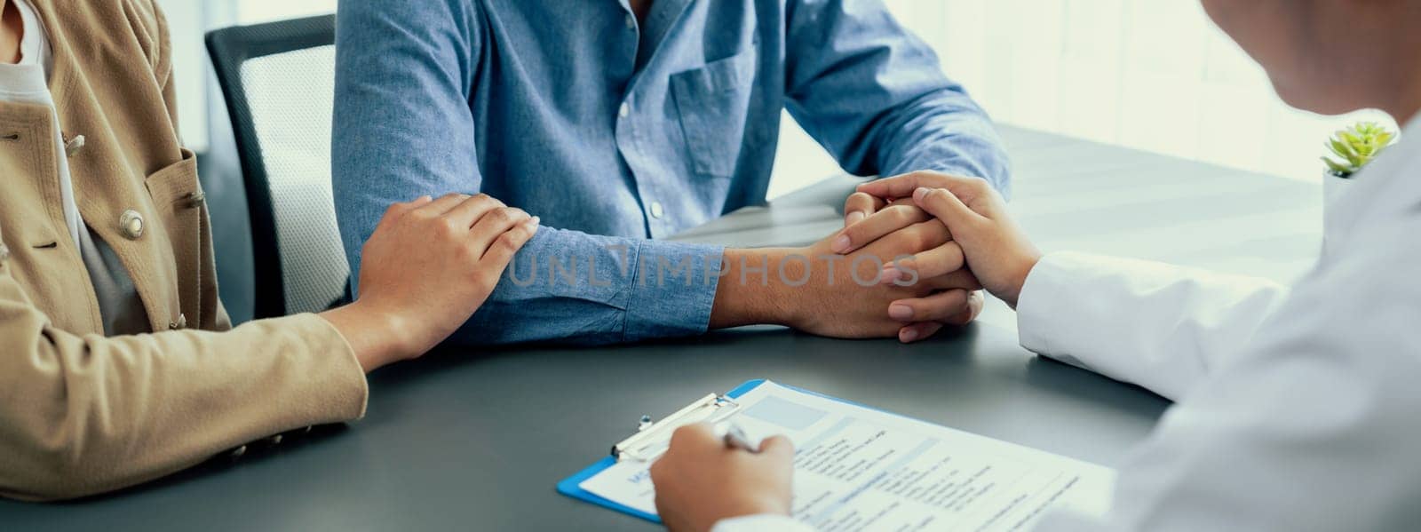 Doctor providing compassionate healthcare consultation while young couple patient holding hand, comfort each other after infertile report. Reproductive and medical fertility consulting. Neoteric