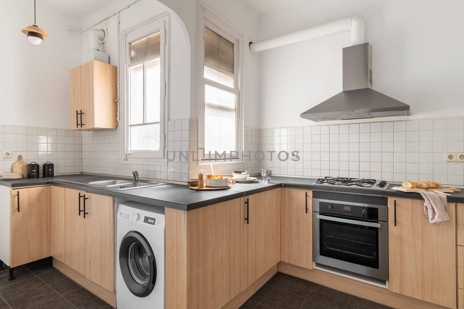 Stylish kitchen with built-in appliances oven and washing machine with extractor hood and white tiles in a modern apartment. Concept of a five-star hotel and spacious kitchen.