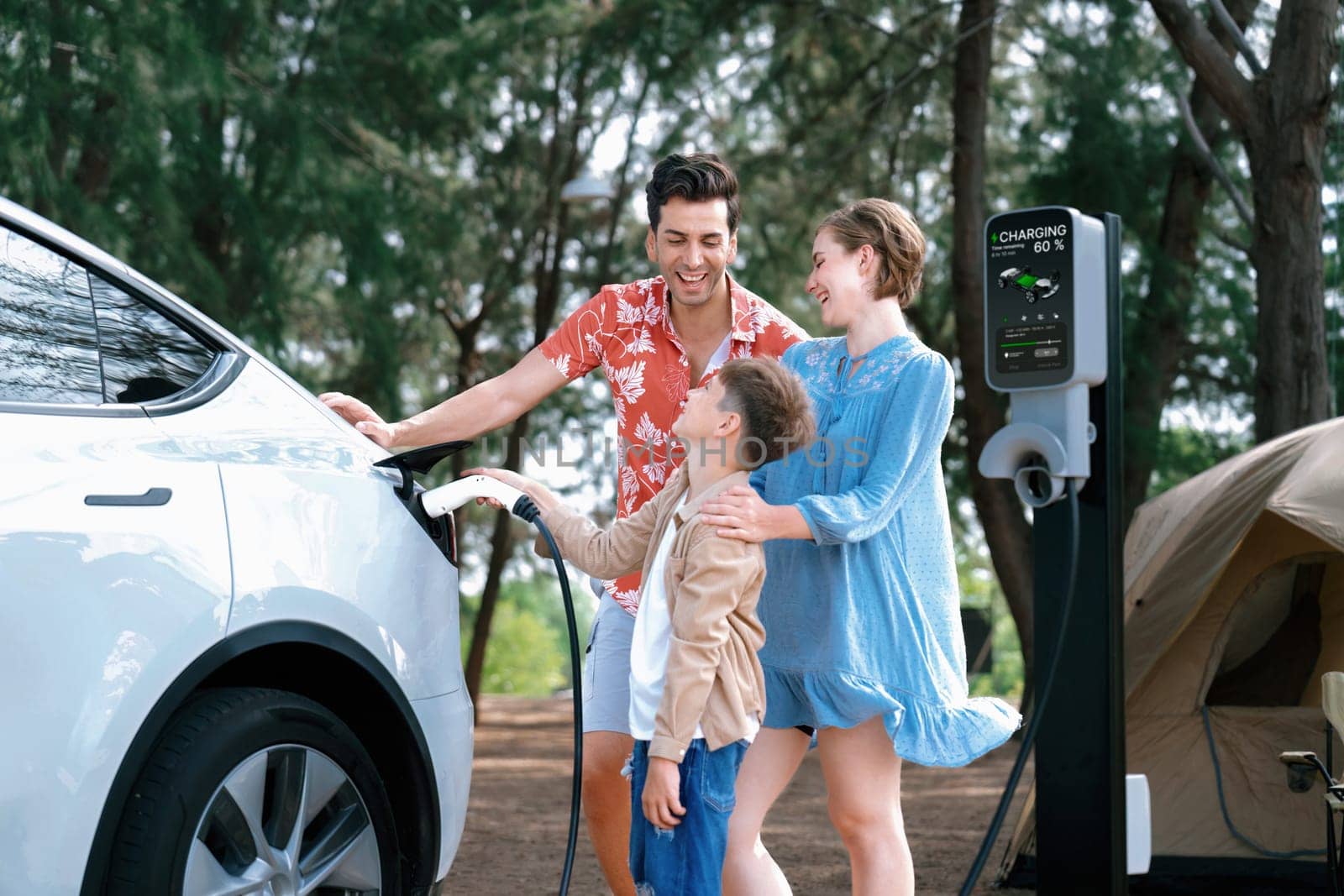 Outdoor adventure and family vacation camping in nature travel by eco friendly car for sustainable future. Lovely family recharge EV car with EV charging station in campsite. Perpetual