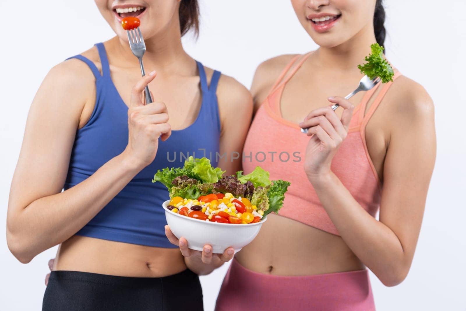 Two young sporty Asian women in sportswear holding salad bowl fill with fruit and vegetable. Natural youthful and fit body lifestyle people with balance nutrition on isolated background. Vigorous