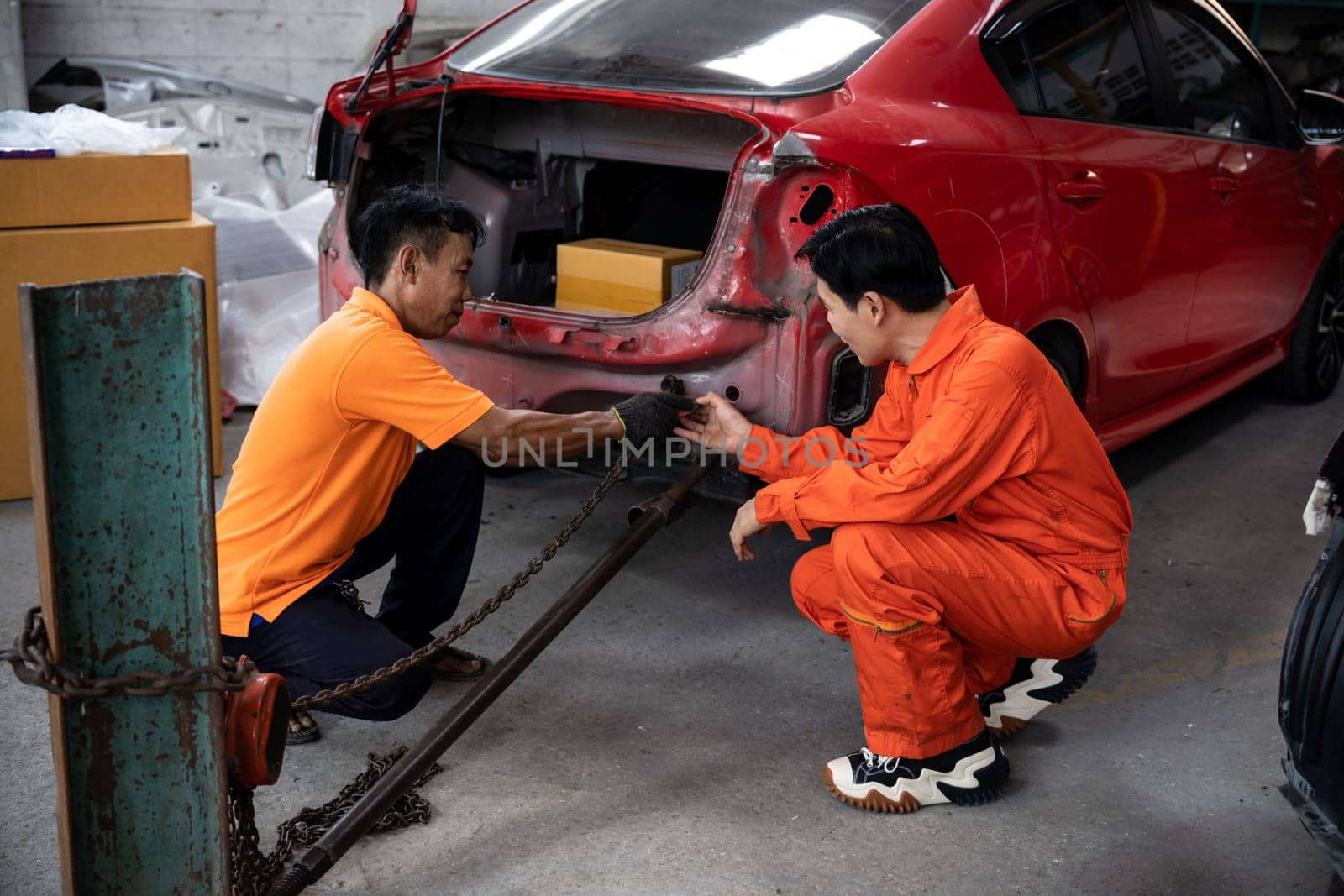 Mechanic testing strength and reliability of chain hoist for car towing in car workshop garage. Automotive service worker ensure through inspection of mechanical equipment. Oxus