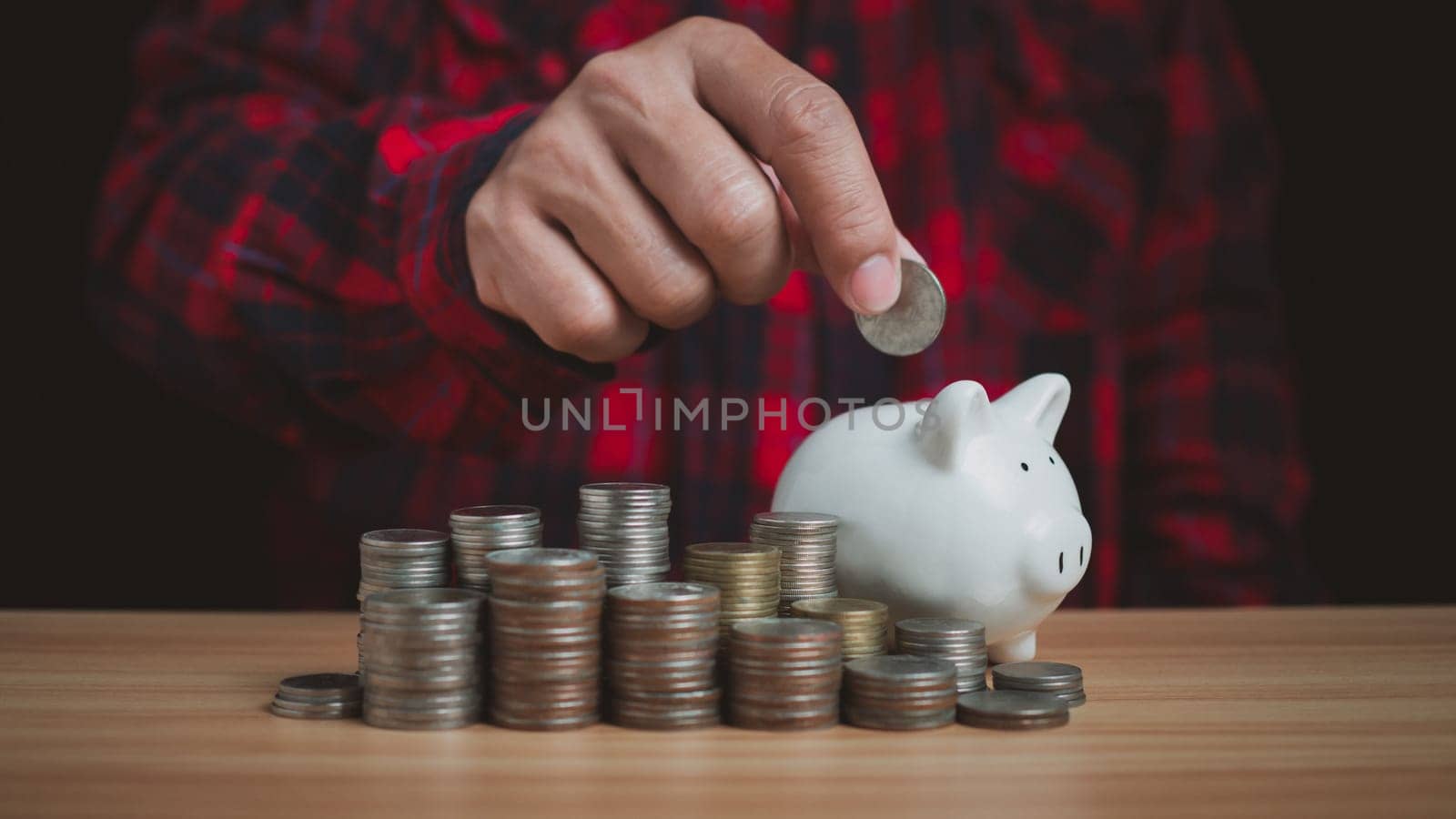 Human puts money on pile of piggy bank. Concepts of finance, savings, investment, and setting goals for fixed deposits with banks.