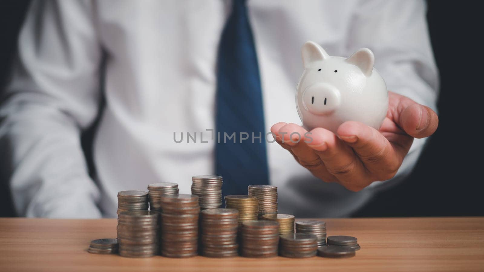 Human holds a piggy bank and there are coins lined up on the wooden floor. Concepts of finance, savings, investment, and setting goals for fixed deposits with banks.