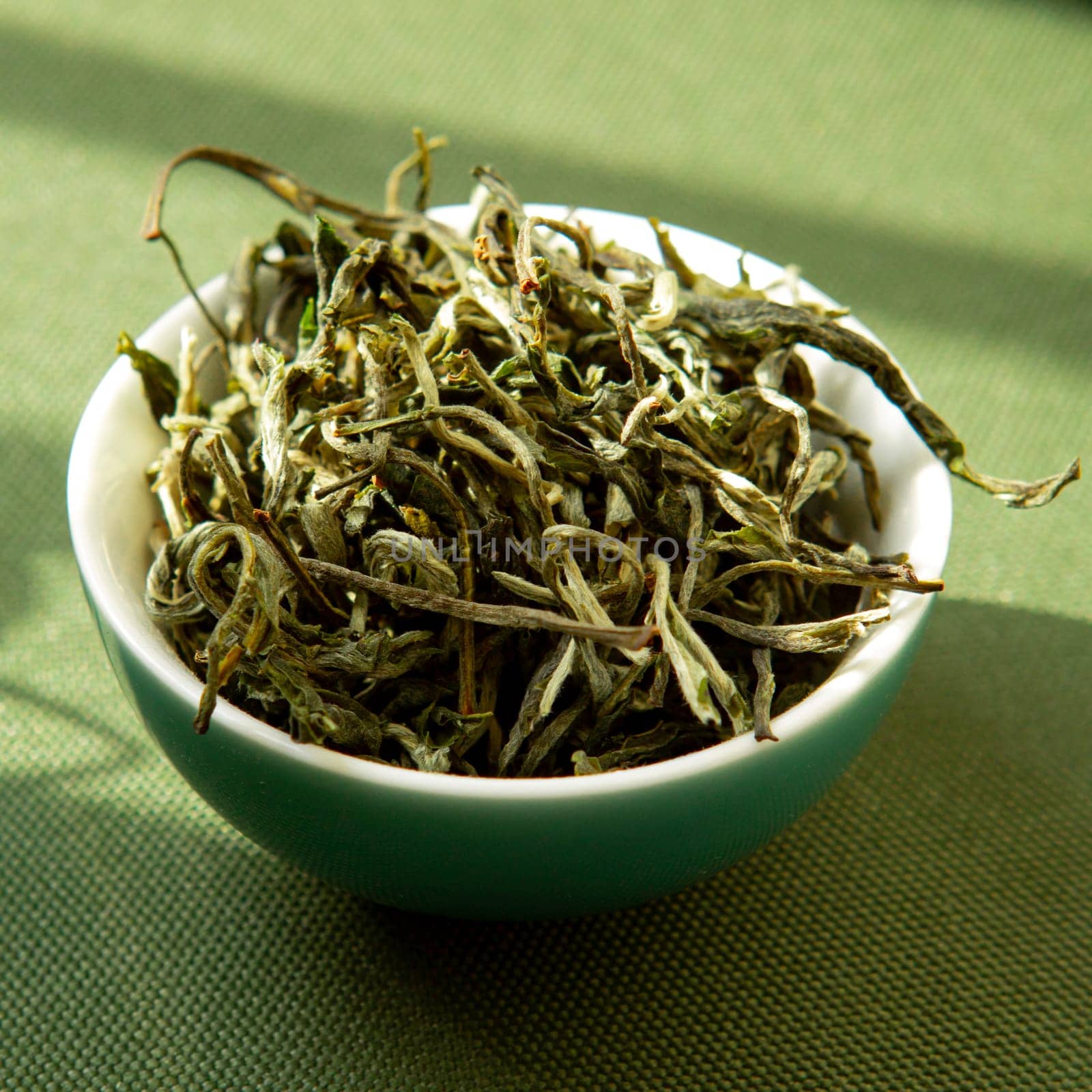 A closeup of vibrant, dried green tea leaves in a bowl, showcasing their beauty and unique texture
