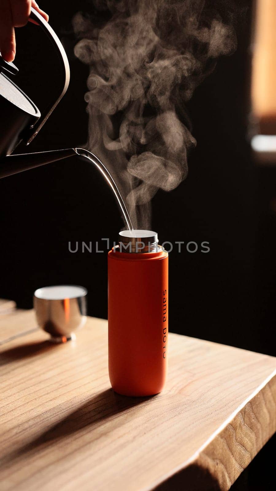 A steaming kettle elegantly pours hot water into a sleek, modern bottle that rests on a wooden surface