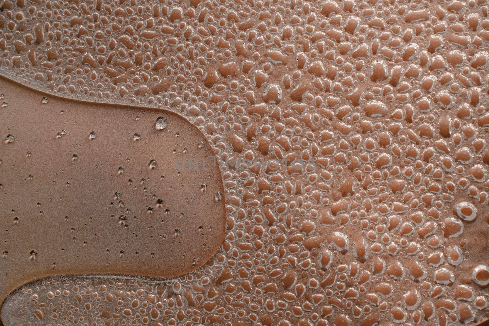 Numerous tiny water droplets condense on a brown surface, creating an intricate textured pattern resembling a natural mosaic, with varying droplet sizes and shapes adding visual interest