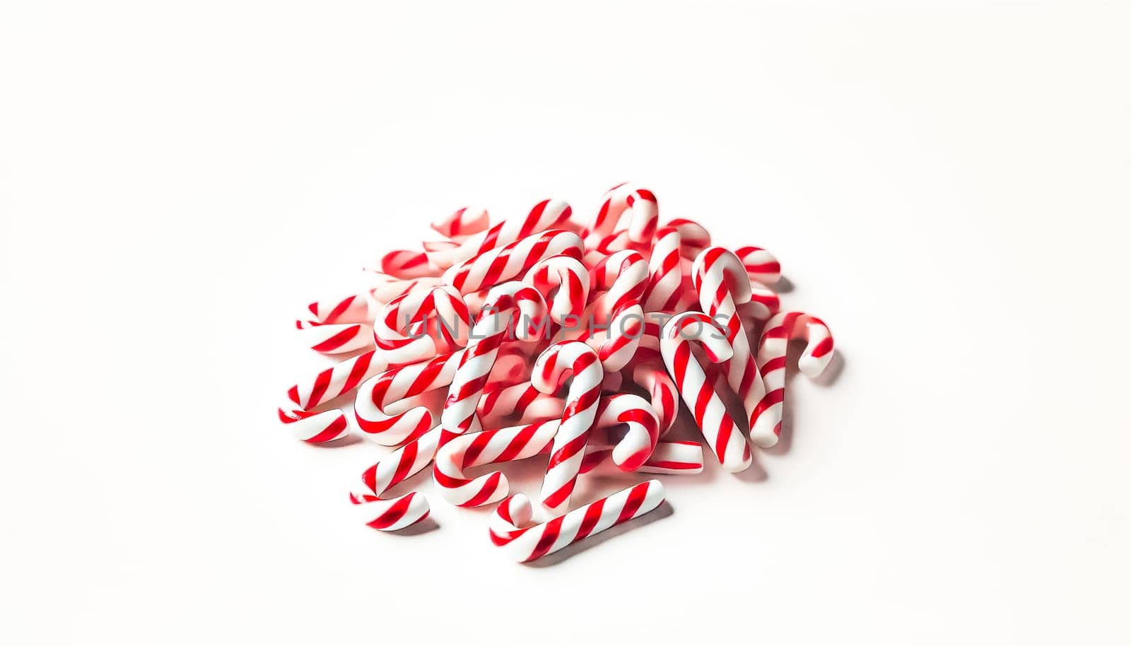 A small pile of neatly rearranged red and white striped candy canes viewed from a slightly elevated angle on a plain white background. This organized heap highlights the candy canes' colorful and festive appearance while maintaining a playful and casual feel.