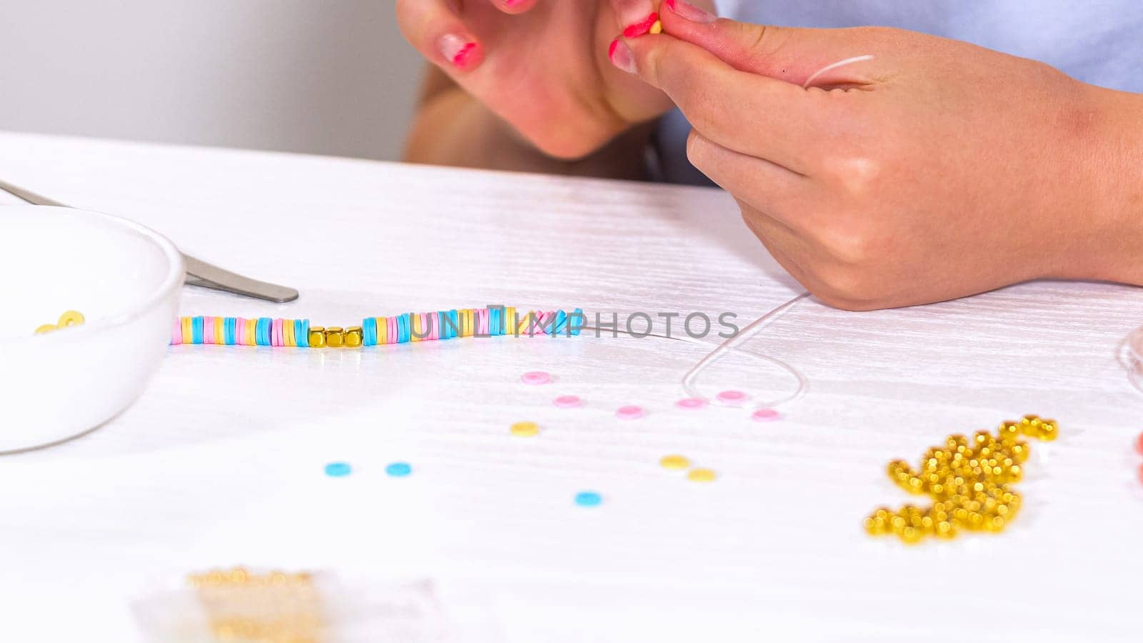 Delicate fingers of a young girl navigate through a treasure trove of bright, multicolored beads, each compartment revealing a new hue to choose from. Shes immersed in the joyful task of stringing together a handmade bracelet, with golden beads and pearls lying nearby to add a touch of sparkle to her creation.