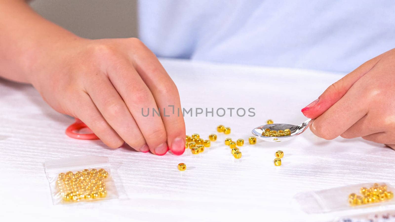 Delicate fingers of a young girl navigate through a treasure trove of bright, multicolored beads, each compartment revealing a new hue to choose from. Shes immersed in the joyful task of stringing together a handmade bracelet, with golden beads and pearls lying nearby to add a touch of sparkle to her creation.