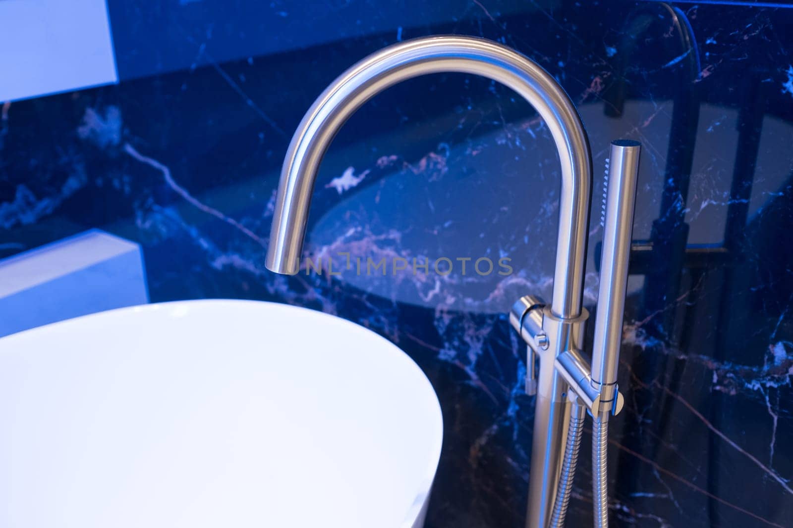 Closeup of silver bathroom faucet in bathroom next to white tub. Chrome faucet against a black granite wall.