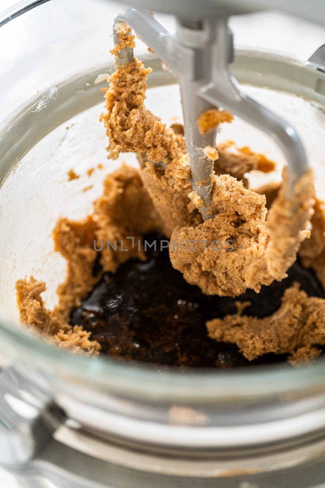 The thick, creamed mixture of butter and sugar is in the mixing bowl. The mixer paddle is beginning to fold the ingredients together, creating a cohesive blend.