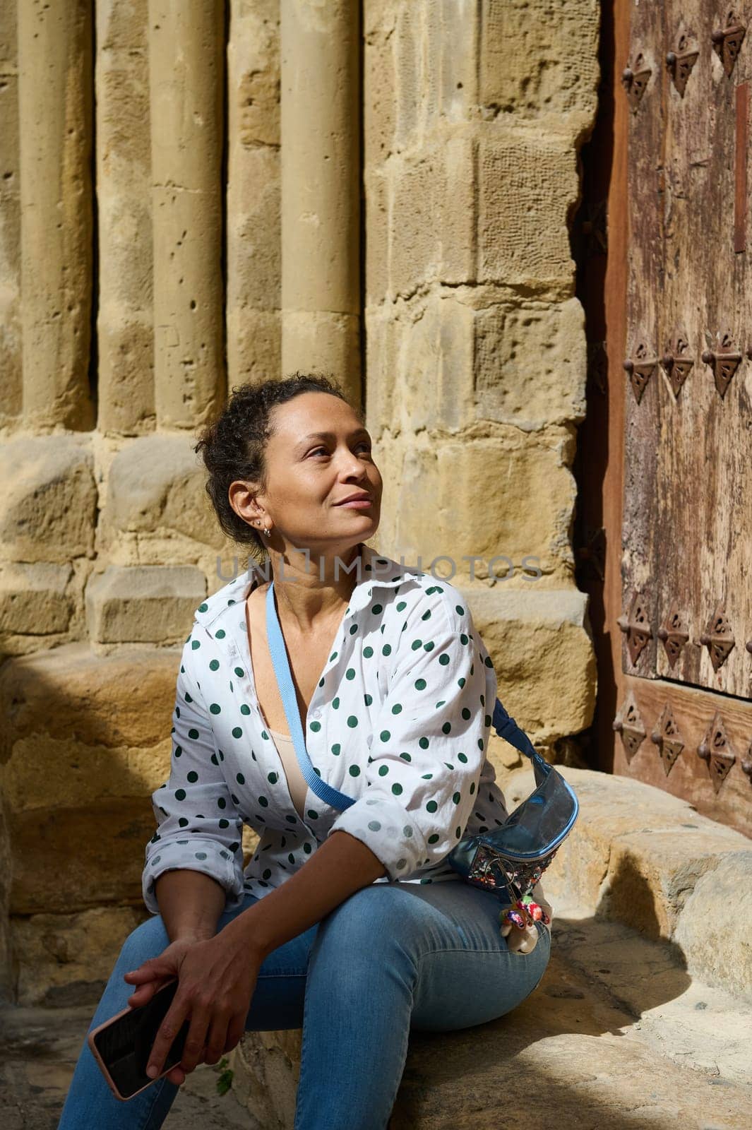 A woman sits in the sun, enjoying a moment of reflection near ancient stone columns.