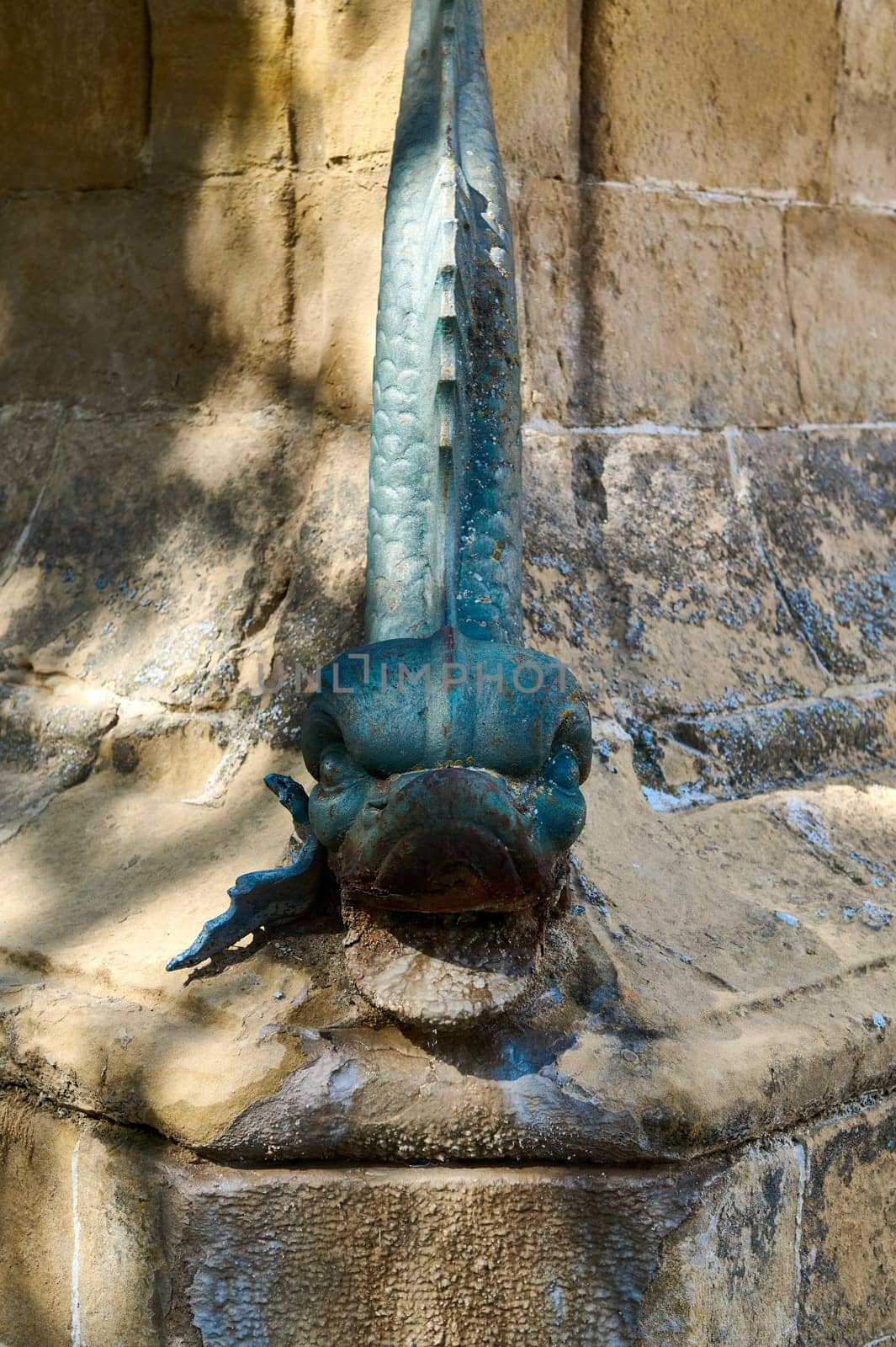 Close-up of a mysterious blue stone gargoyle on a rustic stone wall, highlighting its intriguing texture and detail. Perfect for lovers of historic architecture and mythical creatures.