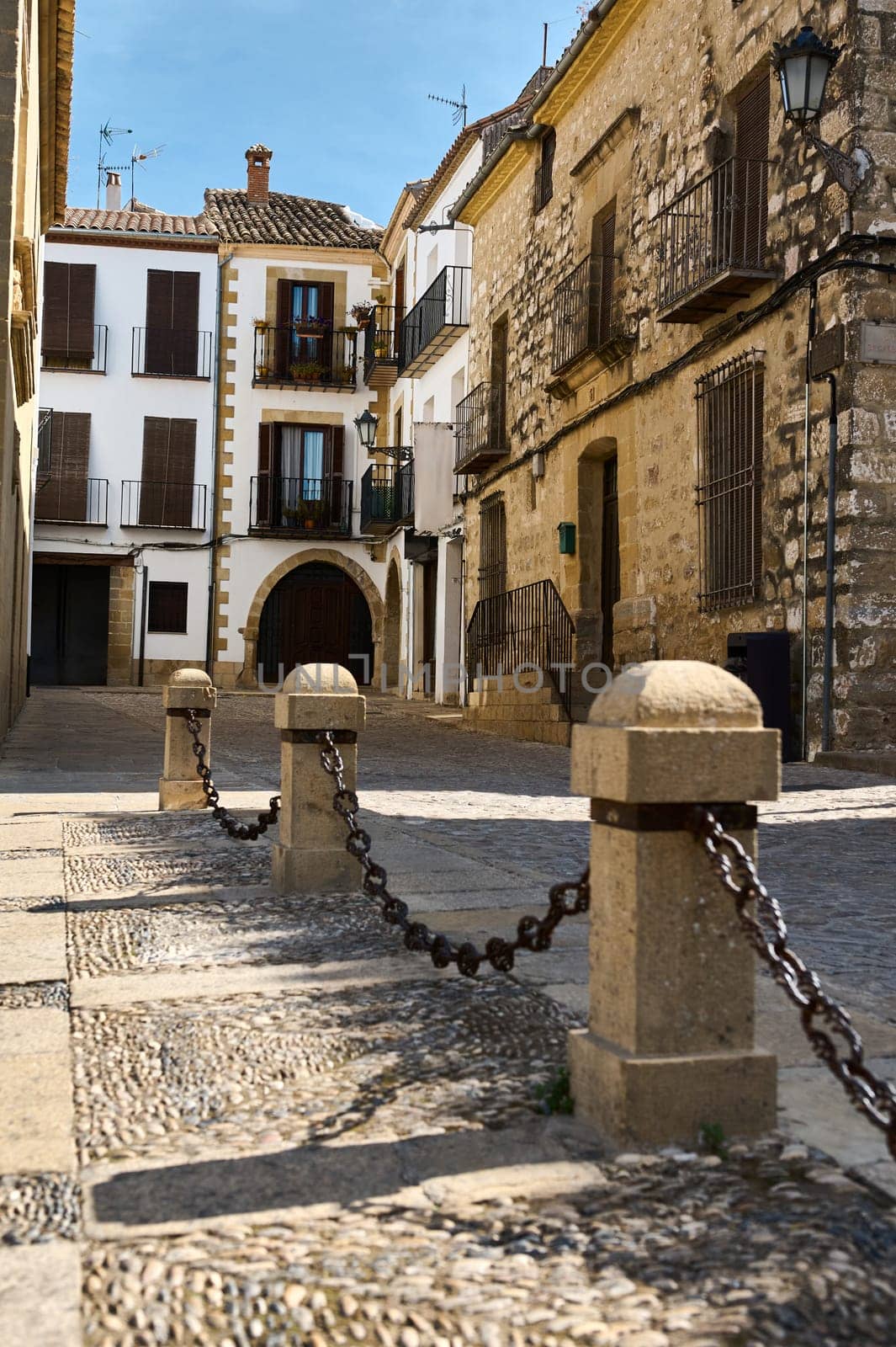 A picturesque cobblestone street features charming historic Mediterranean architecture with balconies. Sunlit and peaceful, it captures the essence of a quaint European village scene.