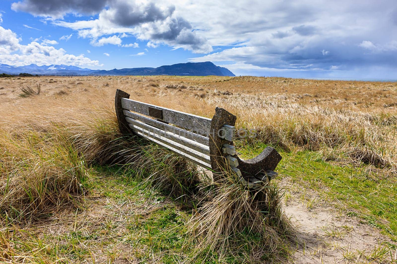 A park bench under a partly cloudy sky on Del Ray beach in Seaside, Oregon.